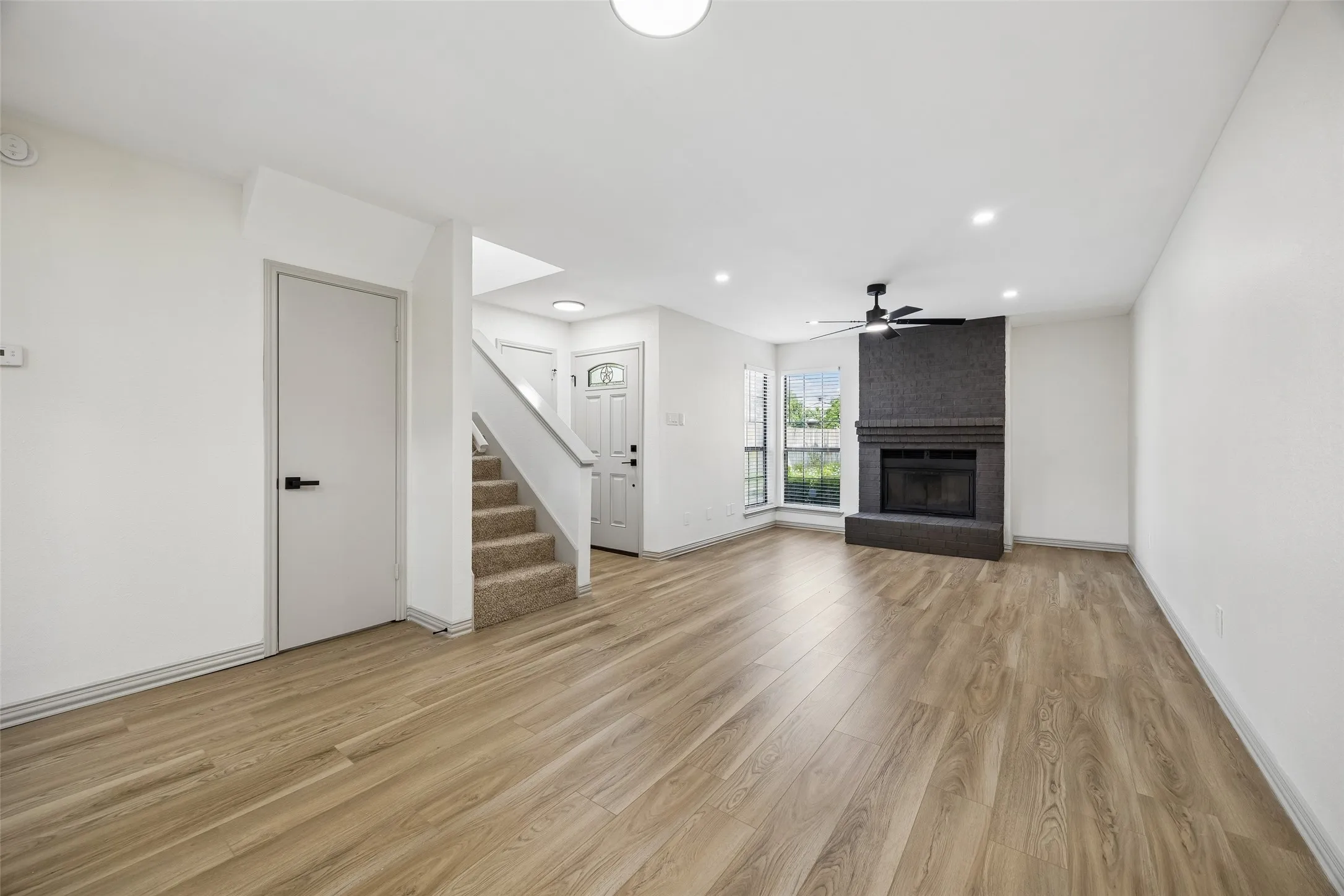 Spacious living area featuring wood-finish flooring, a textured fireplace with a dark surround, and a ceiling fan