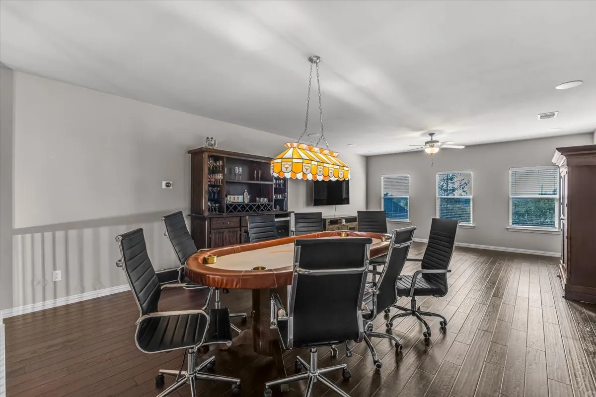 Wood-finish flooring throughout, multiple windows with blinds, a ceiling fan, and a built-in cabinetry unit