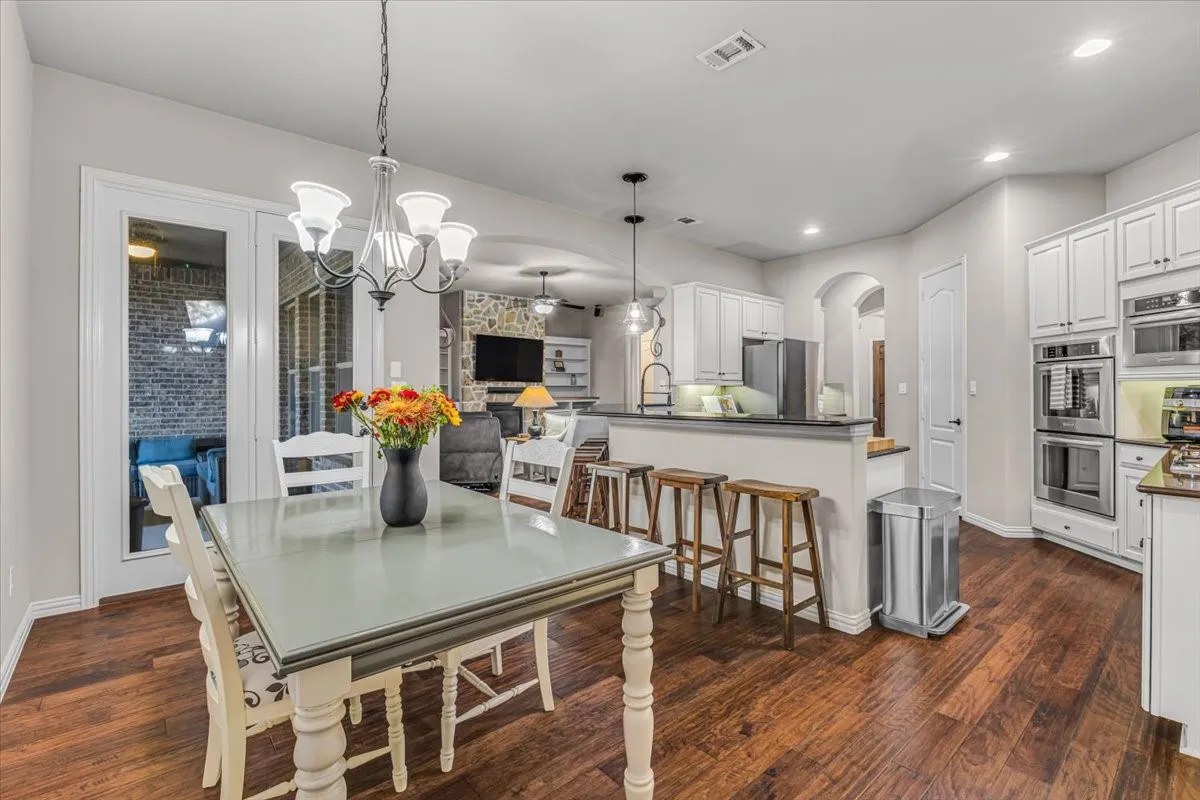 Wood-finish flooring throughout, white cabinetry, built-in double oven, archway, and glass French doors