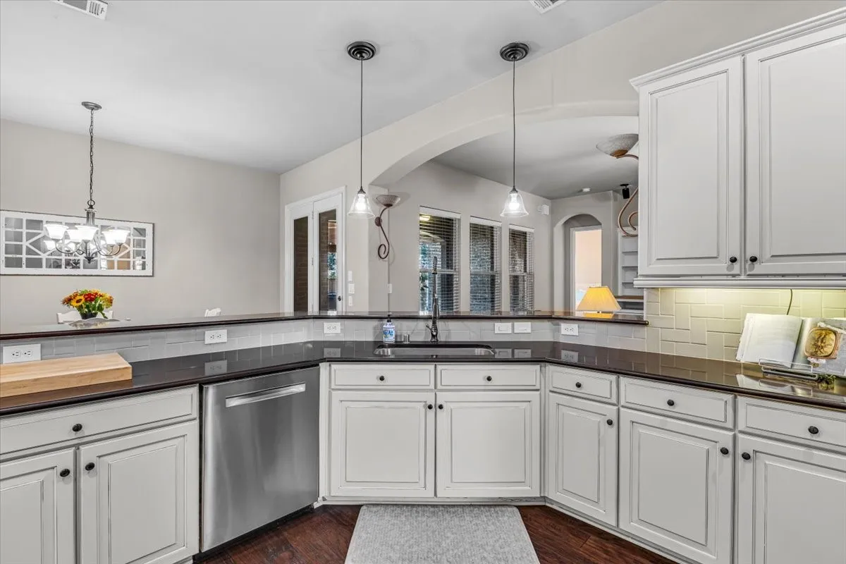 White cabinetry, stainless steel dishwasher, dark countertops, subway tile backsplash, and wood-finish flooring