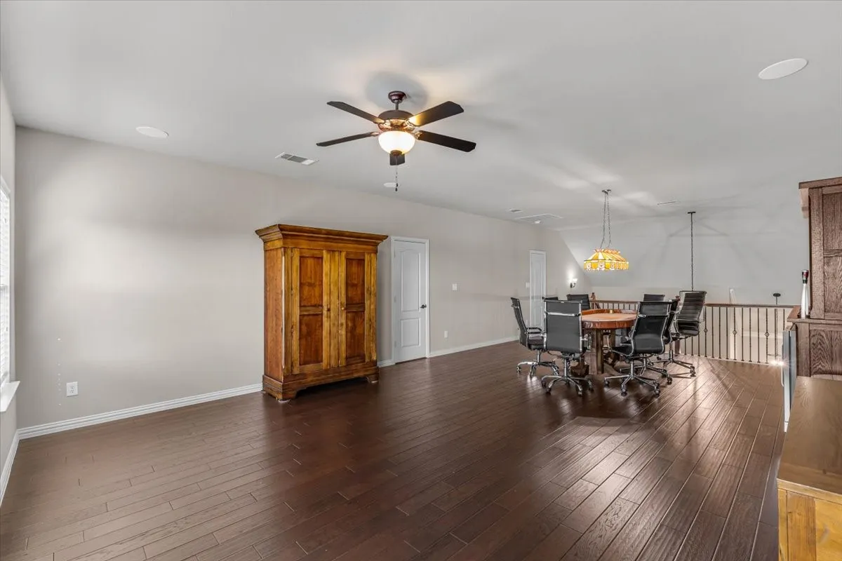 Expansive game room with dark wood-finish flooring, recessed lighting, and a ceiling fan with integrated lighting
