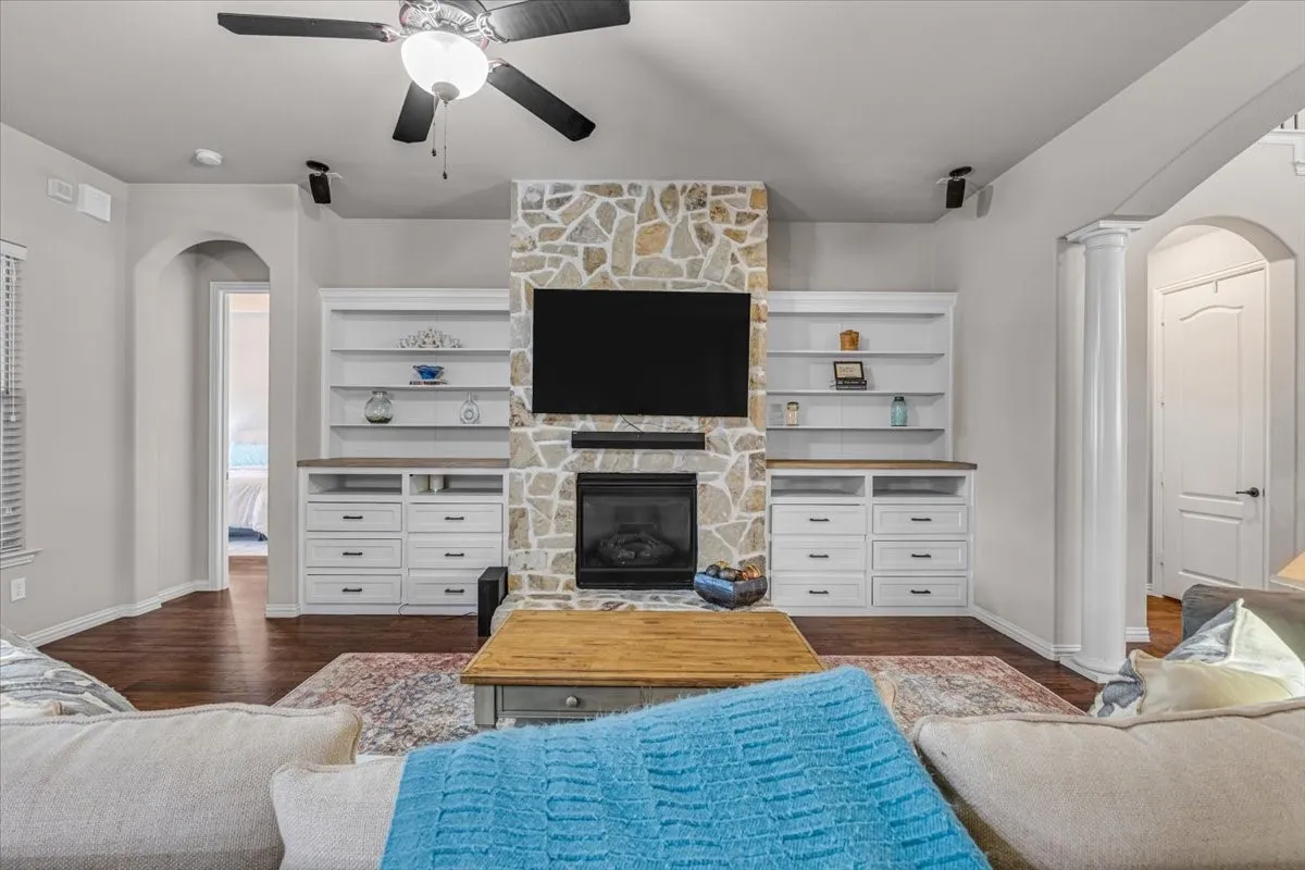 Living area featuring a stone fireplace, built-in cabinetry, wood-finish flooring, and arched doorways