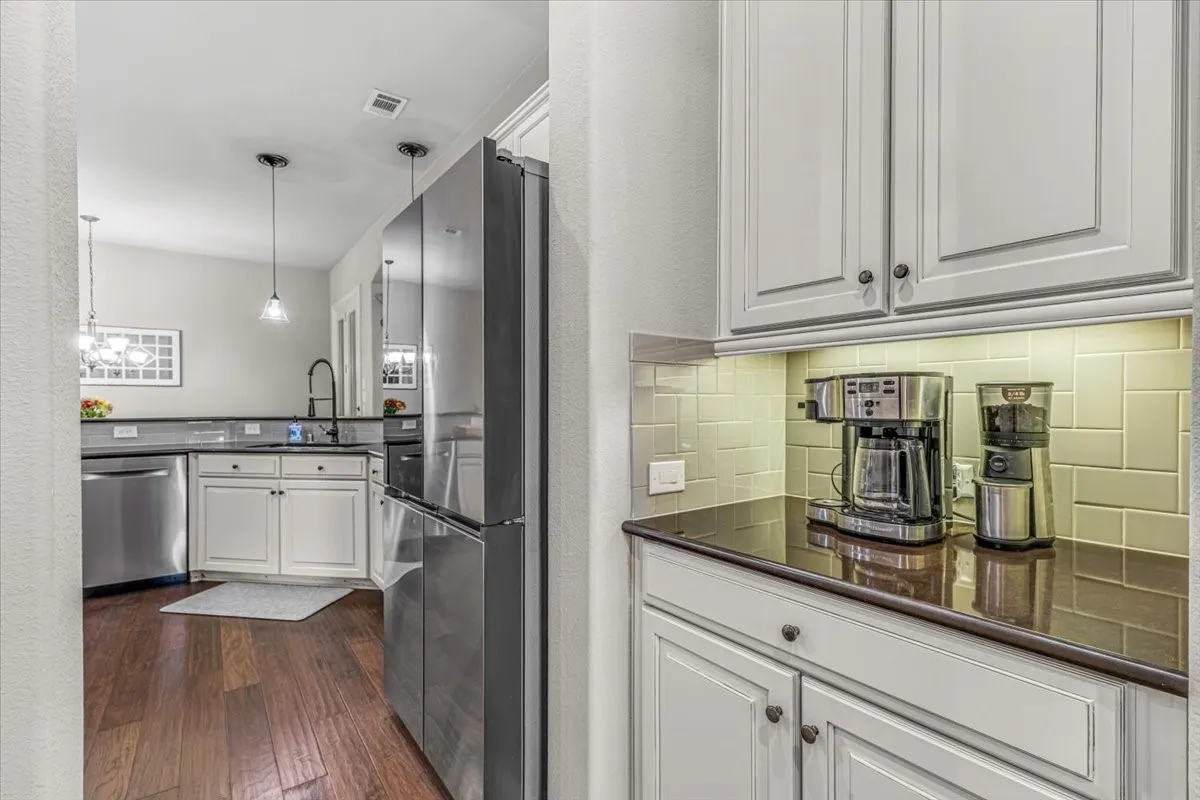 White shaker-style cabinetry with dark hardware, dark countertops, tile backsplash, and wood-finish flooring