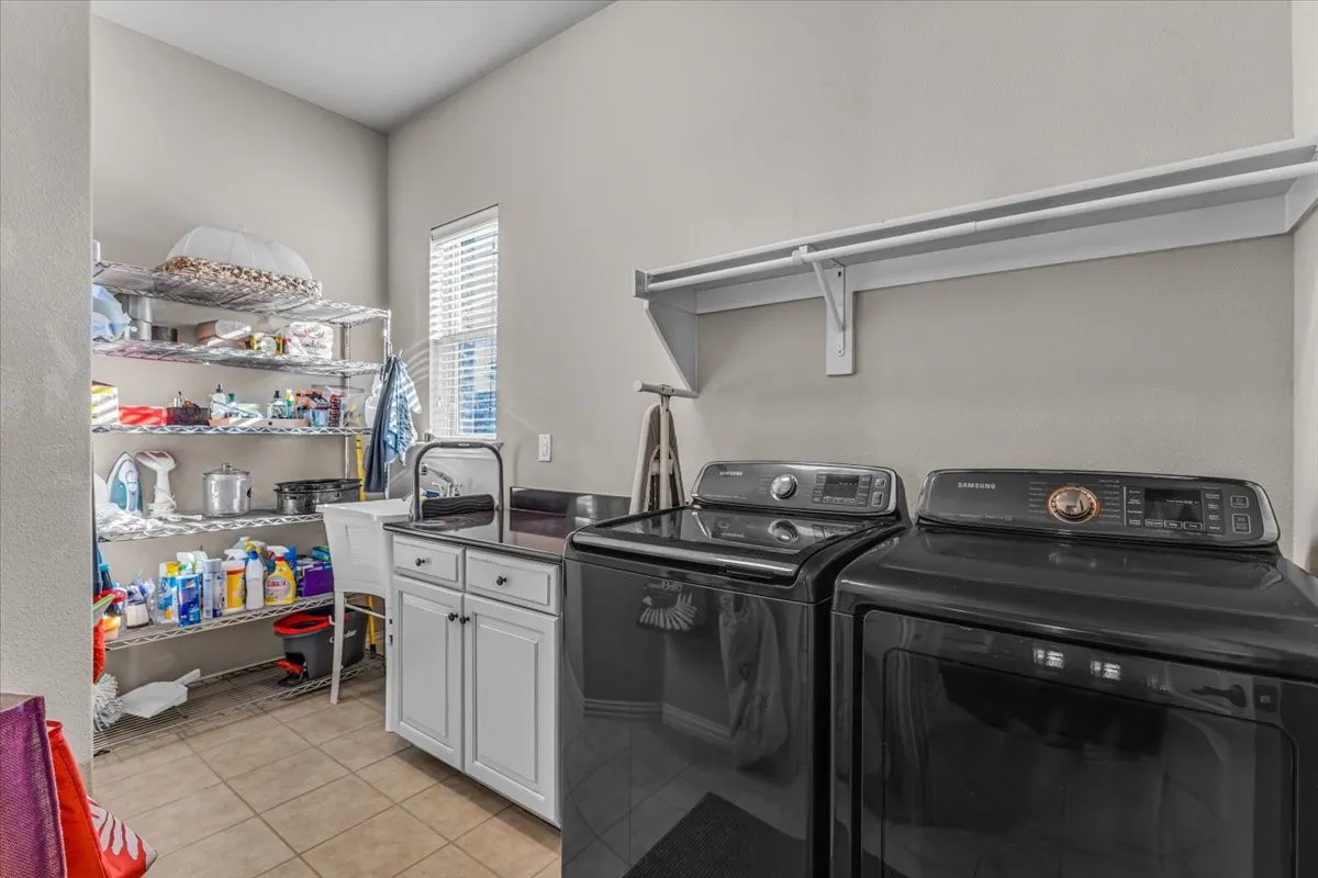 Laundry area with tile flooring, built-in shelving, white cabinetry, dark countertop, and utility sink