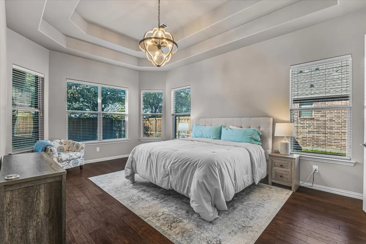 Tray ceiling with a decorative chandelier, wood-finish flooring, and multiple windows