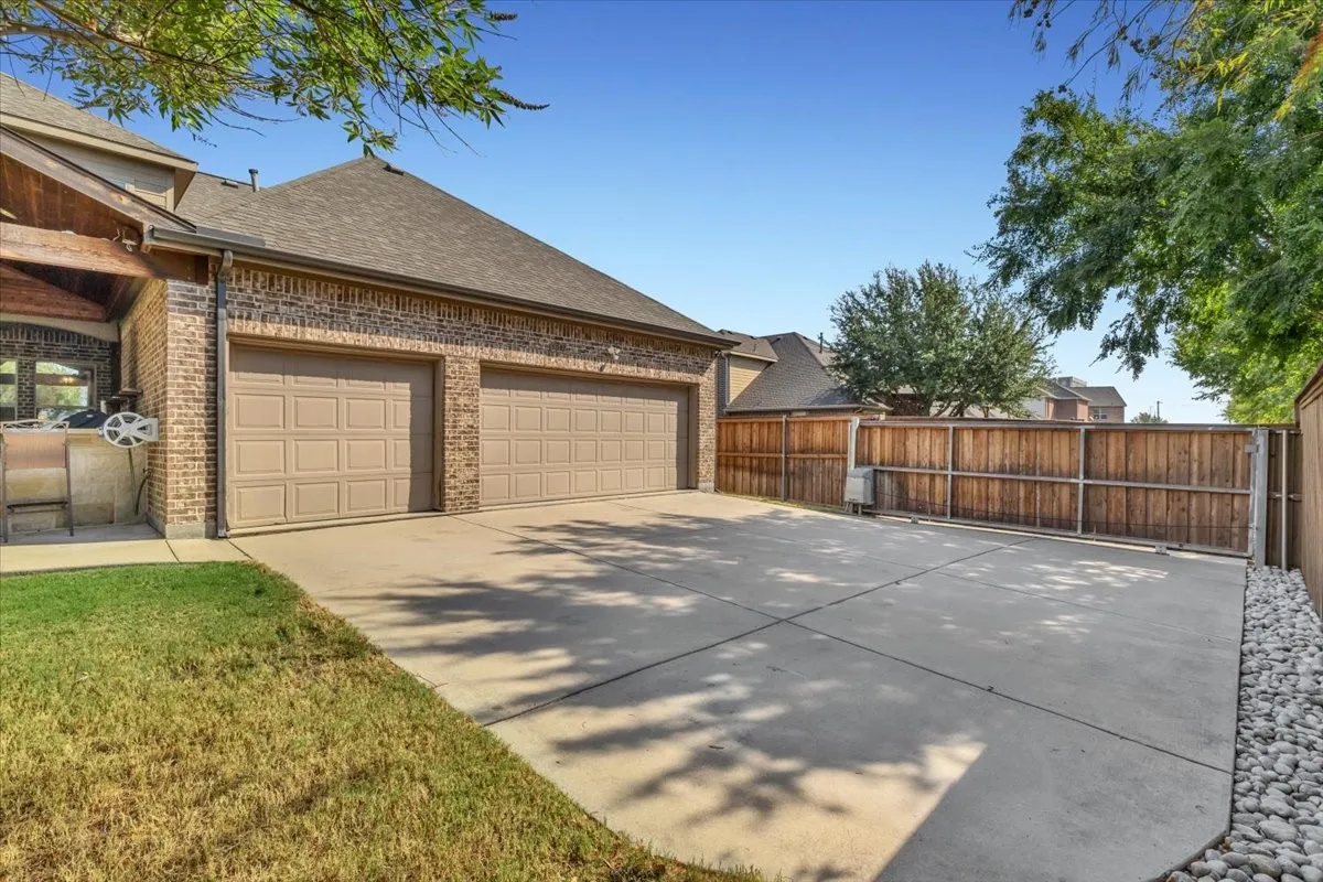 Three-car garage with panel doors, brick exterior, concrete driveway, and wood privacy fence