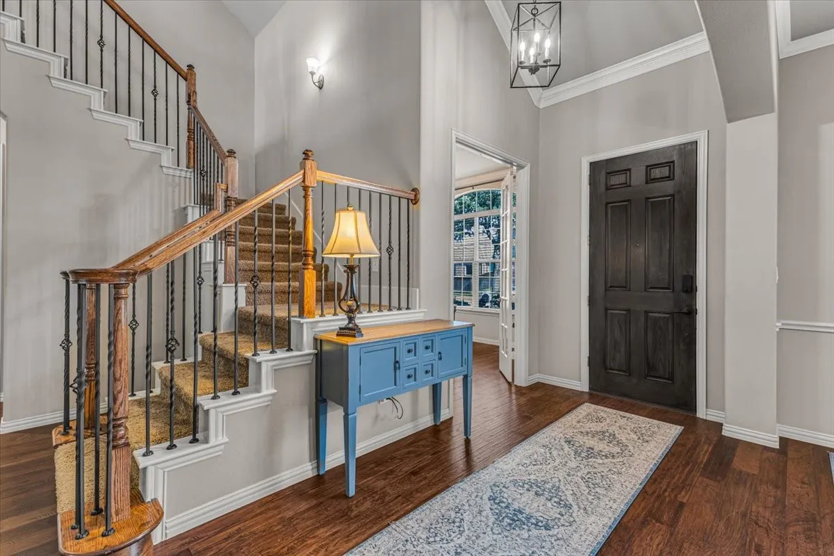 Hardwood-finish flooring, staircase with carpeted treads, wrought iron and wood banister, dark panel entry door, and recessed light fixture