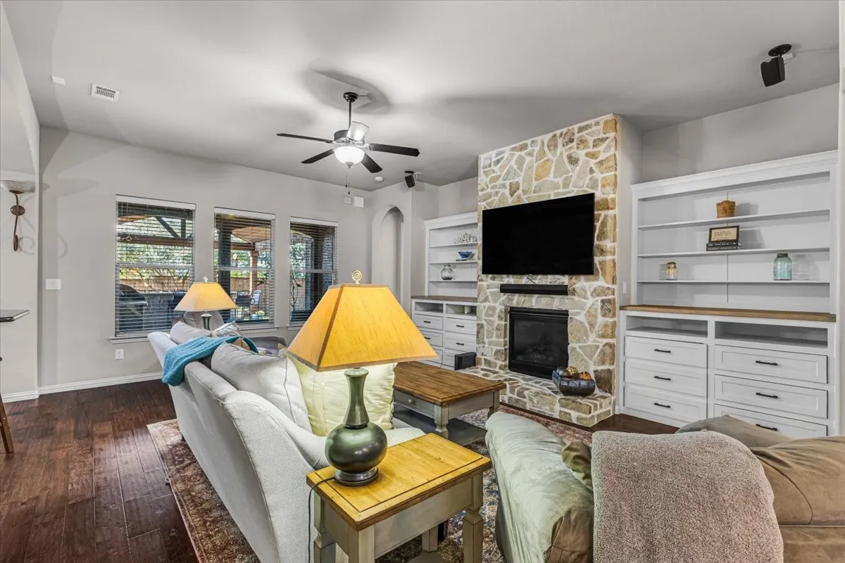 Stone-clad fireplace with built-in shelving, rich wood-finish flooring, and multiple windows
