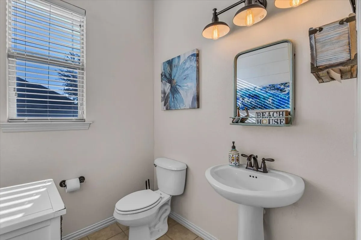 Half bathroom with pedestal sink with a bronze-finish faucet, wall-mounted mirror, three-light vanity fixture, and a window with blinds
