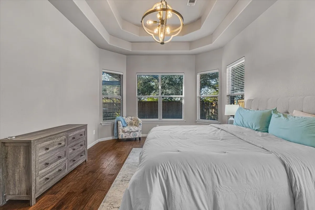 Tray ceiling with a decorative chandelier, multiple windows, dark wood-finish flooring, and light wall finishes