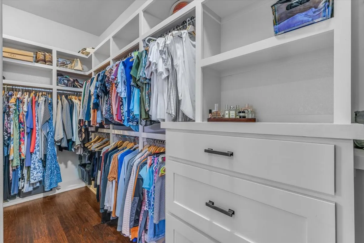 Custom closet system featuring wood-finish flooring, white built-in shelving, and drawers with dark hardware