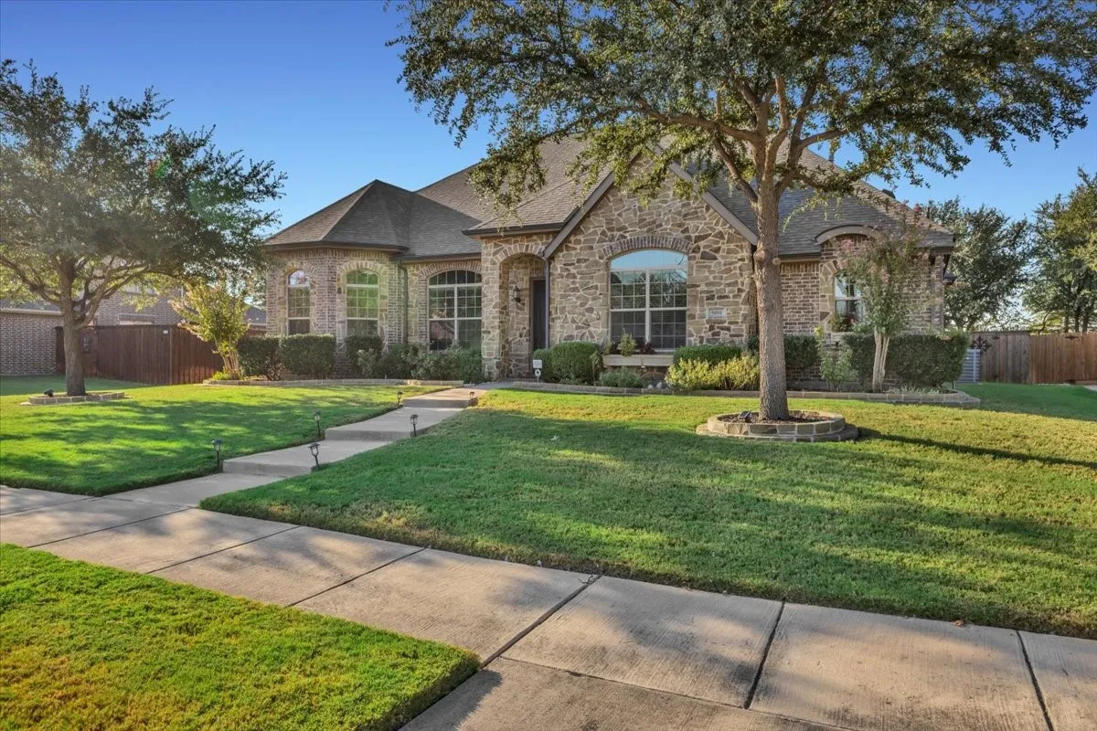 Stone and brick exterior with arched windows, prominent front lawn, mature trees, and a concrete walkway with integrated lighting