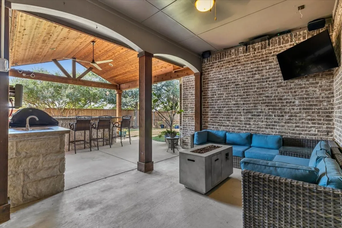 Covered patio with a wood-plank ceiling, exposed wood beams, and a built-in outdoor kitchen with a sink