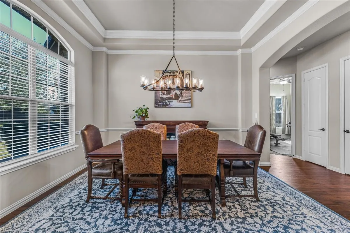 Tray ceiling with crown molding, arched window with white blinds, wood-finish flooring, and an arched doorway