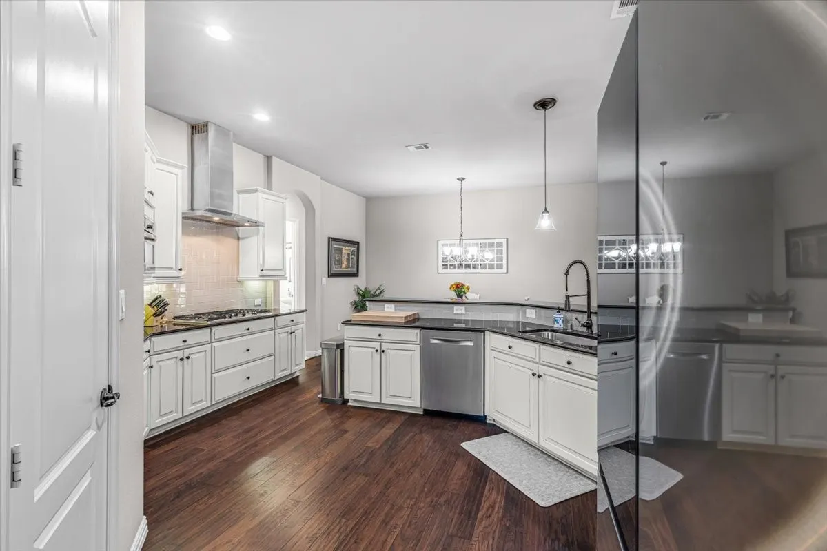 Kitchen featuring white cabinetry, dark countertops, wood-finish flooring, stainless steel appliances, and a tiled backsplash