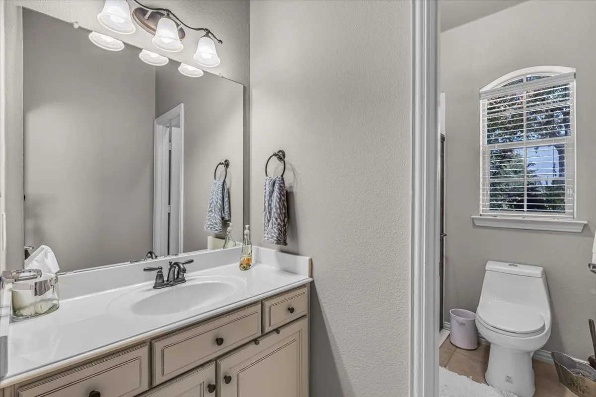 Single vanity with white countertop, undermount sink, bronze-finish faucet, and wood-finish cabinetry