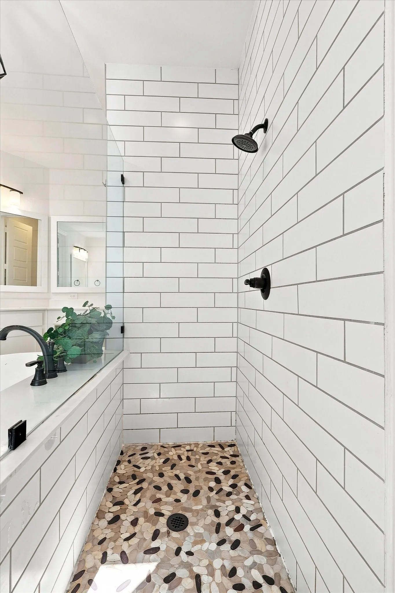 Shower enclosure with white subway tile walls, a river rock floor, and matte black fixtures