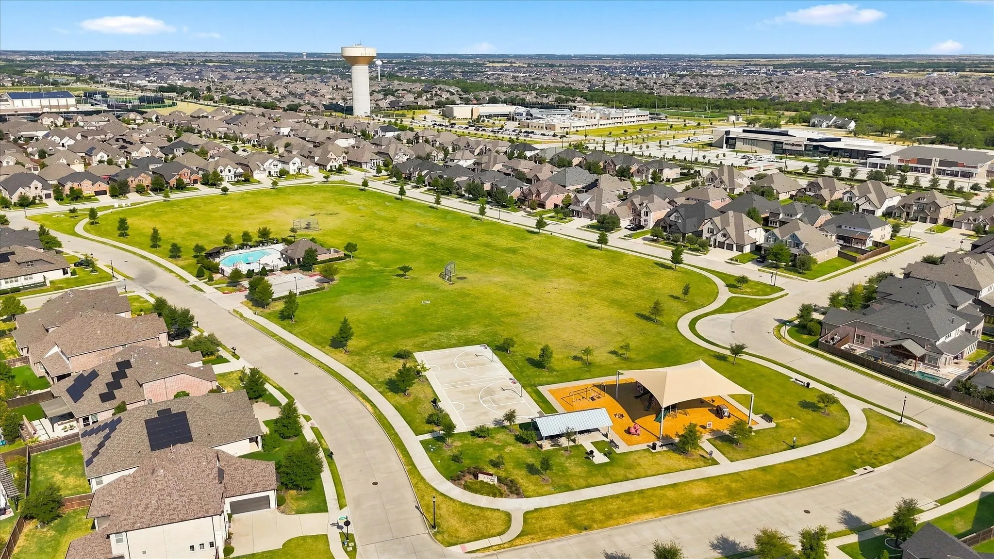 Expansive green space featuring a playground with shade structure, basketball court, and community pool