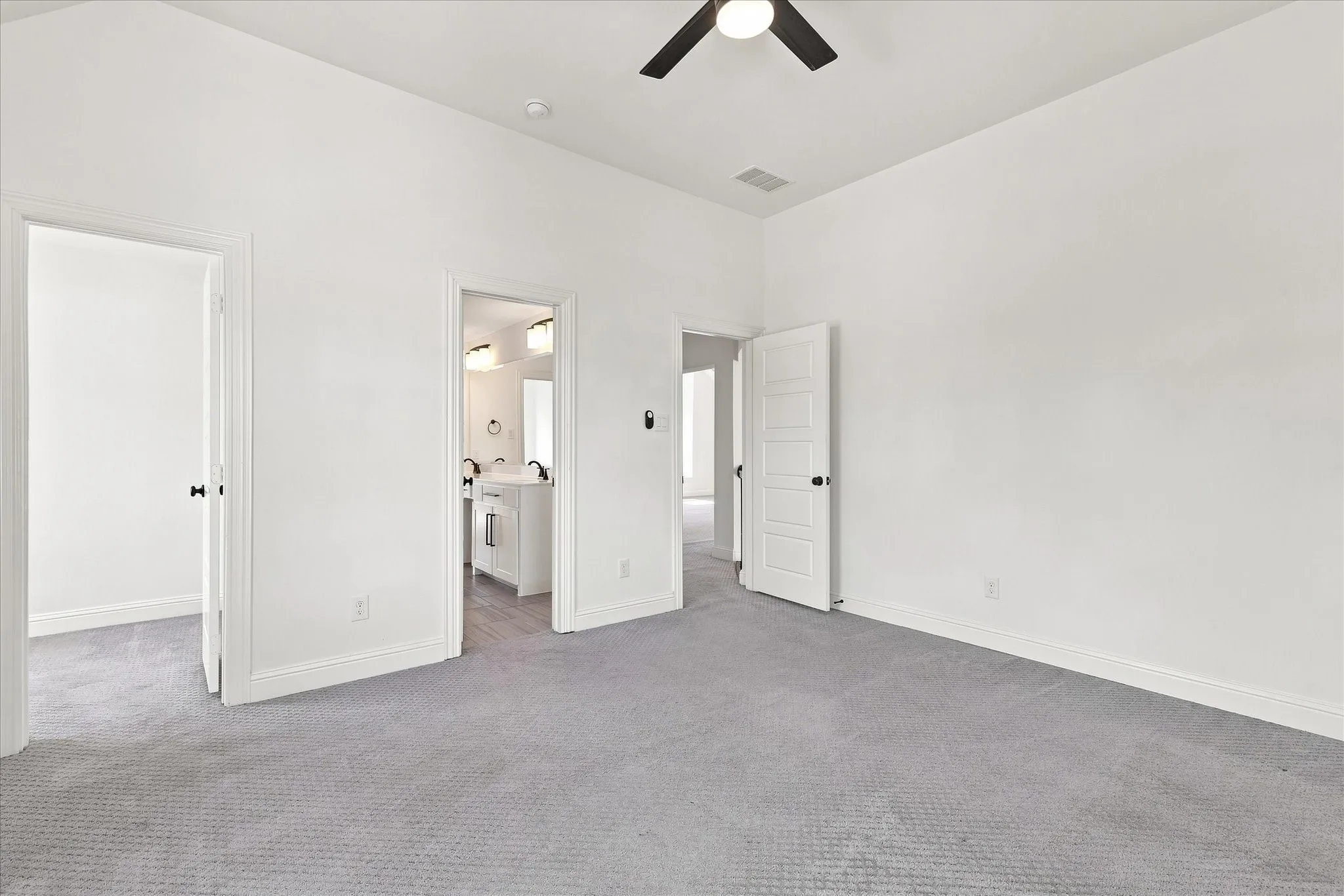 Spacious room featuring light grey carpeting, crisp white walls, multiple doorways with panel doors, and a ceiling fan with integrated lighting