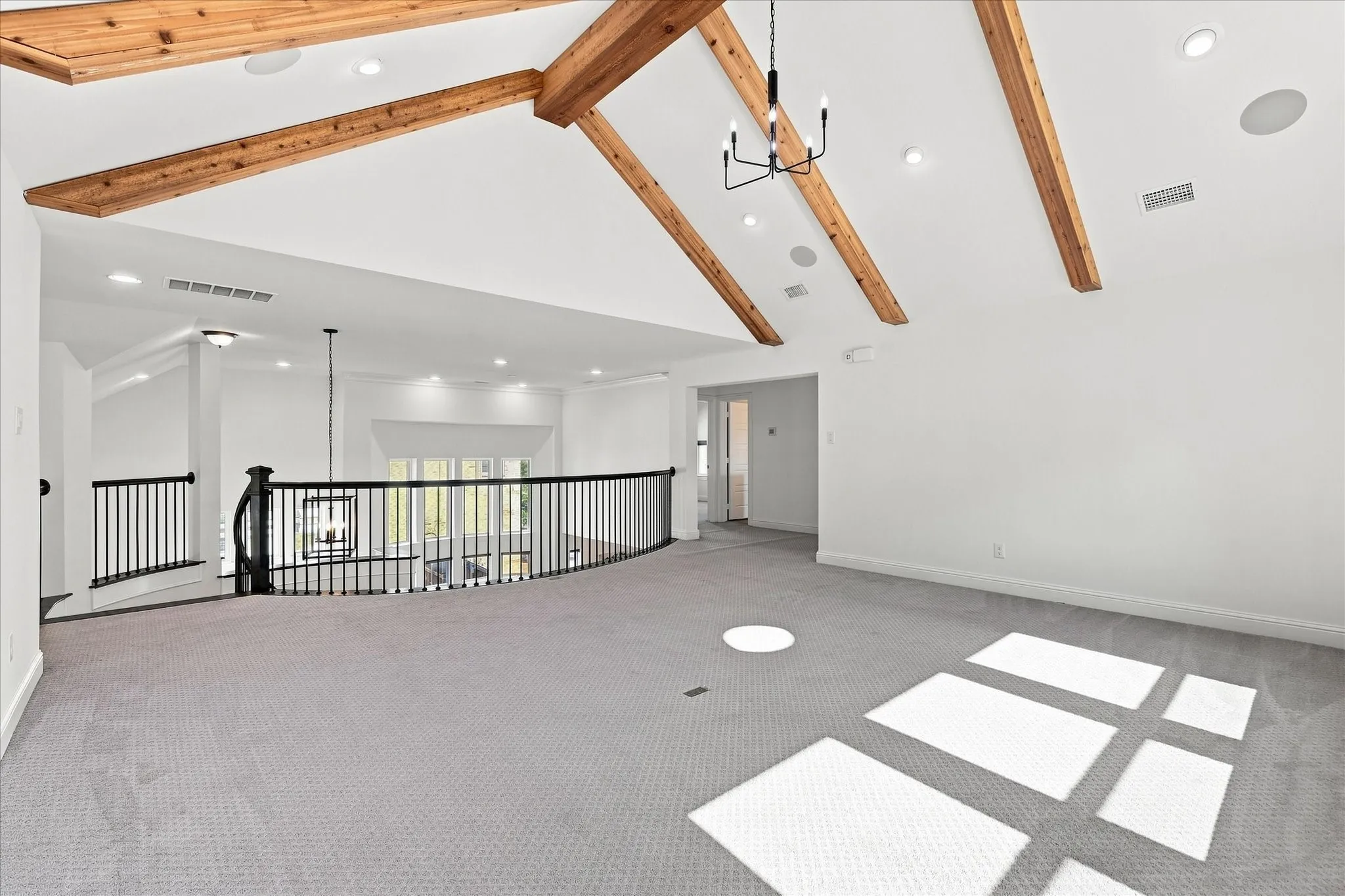Vaulted ceiling with exposed wood beams, recessed lighting, and a modern chandelier