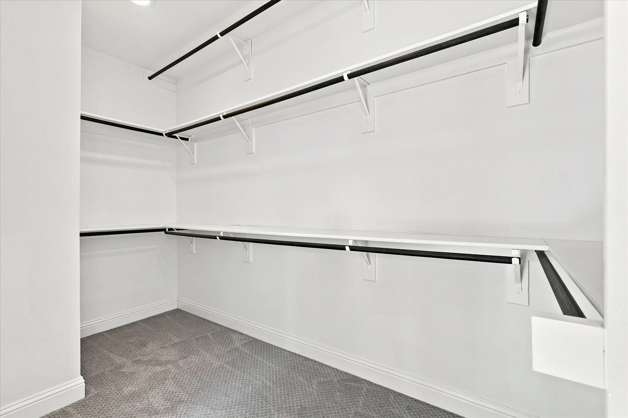 Recessed lighting illuminates a walk-in closet featuring built-in shelving and hanging rods
