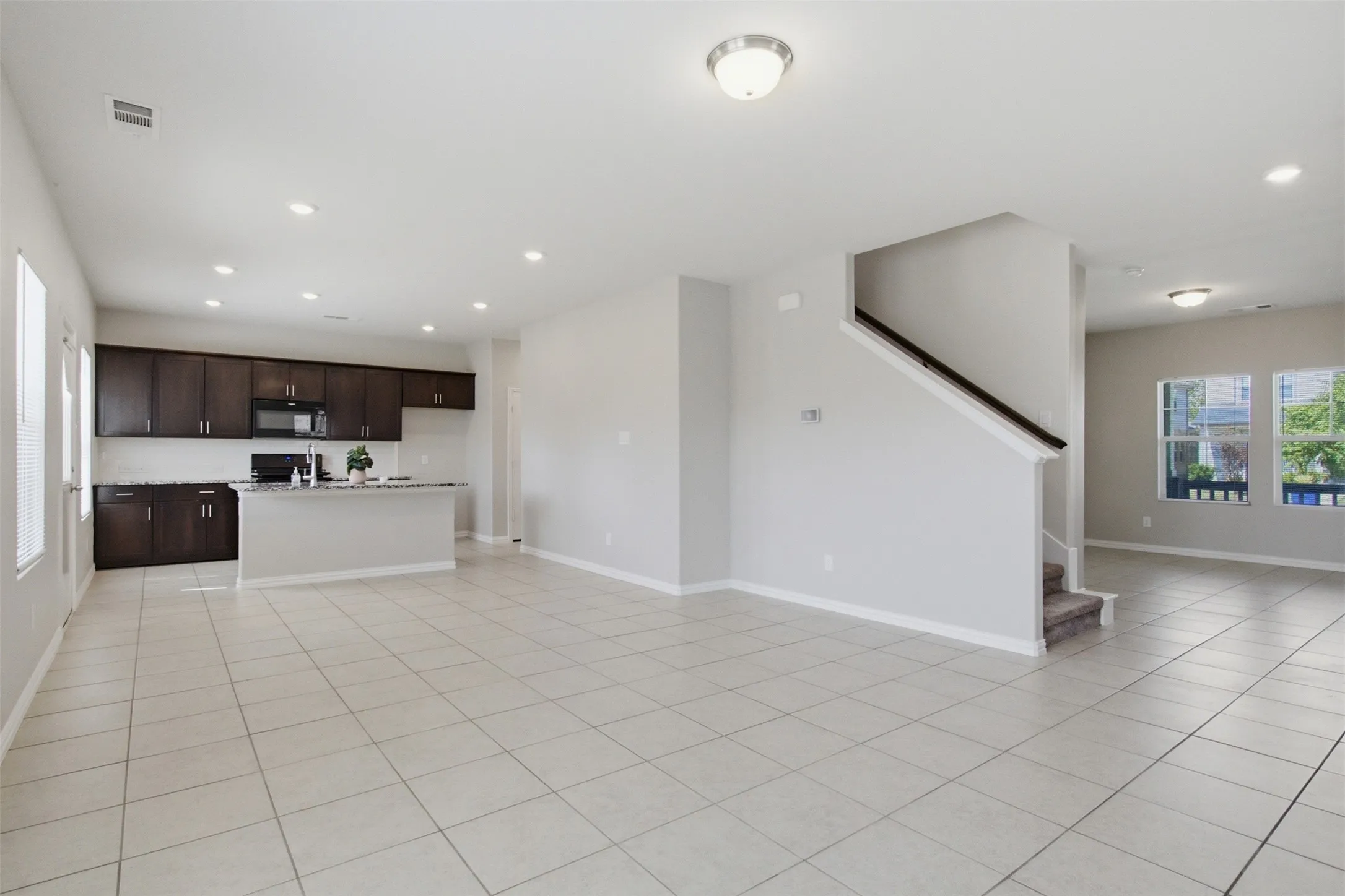 Expansive tiled flooring throughout, kitchen with dark wood-finish cabinetry, built-in microwave, and an island with a countertop