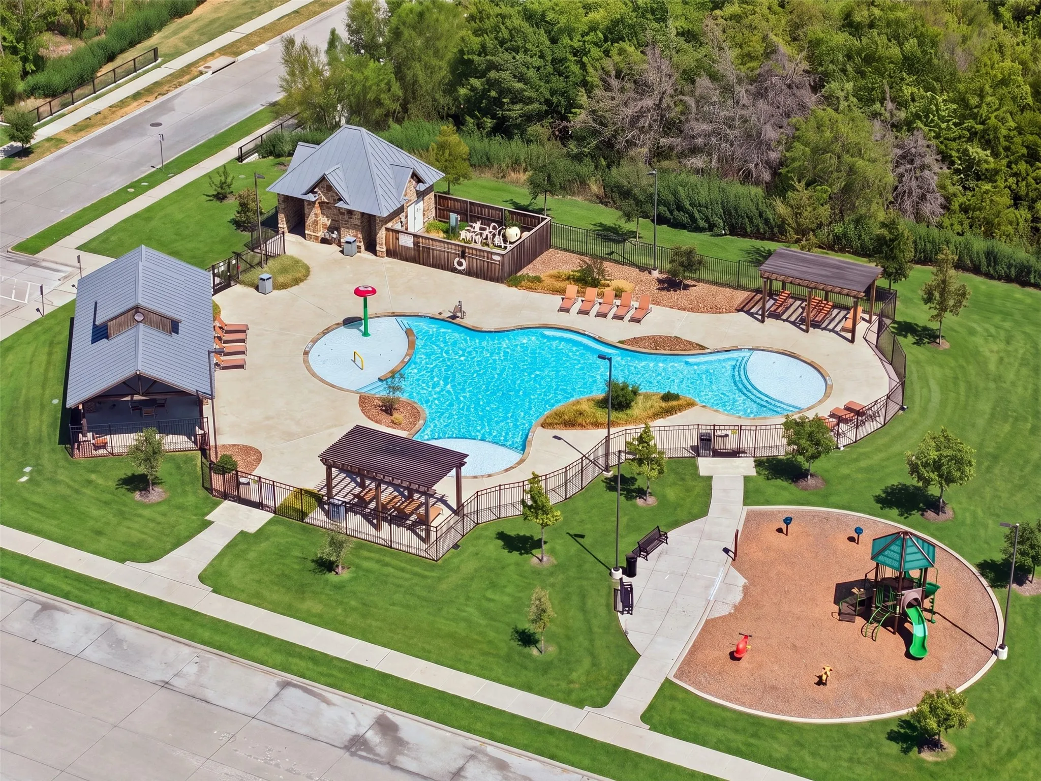 Community pool with integrated splash pad, two covered pergolas, and adjacent playground structure