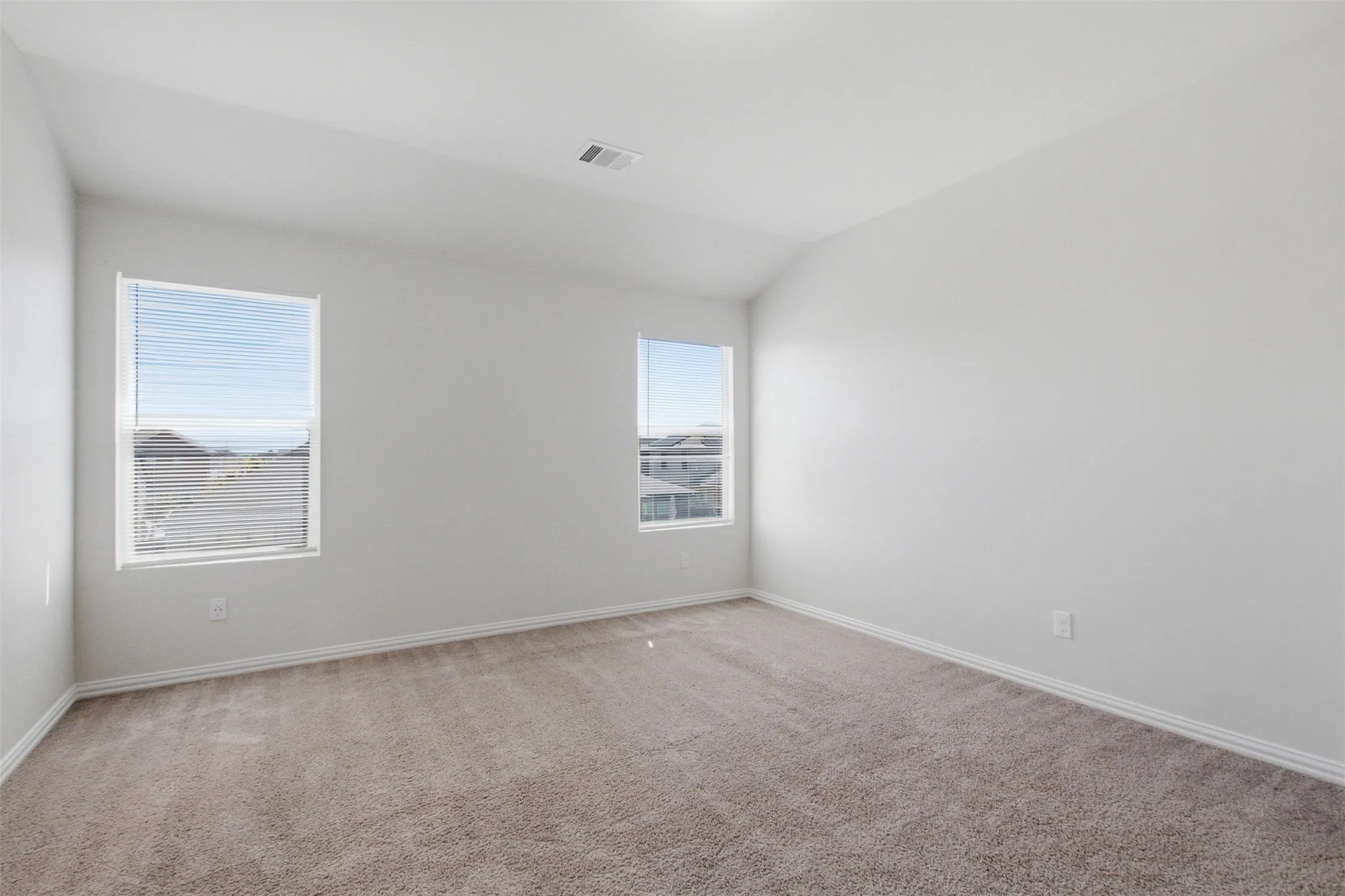 Neutral tone wall paint, vaulted ceiling, two windows with blinds, and carpeted flooring