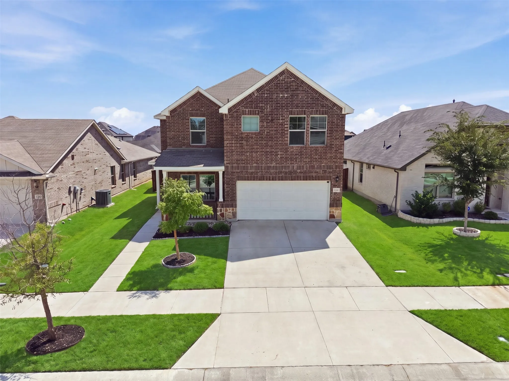 Brick exterior with a covered entry, attached garage, concrete driveway, and manicured landscaping