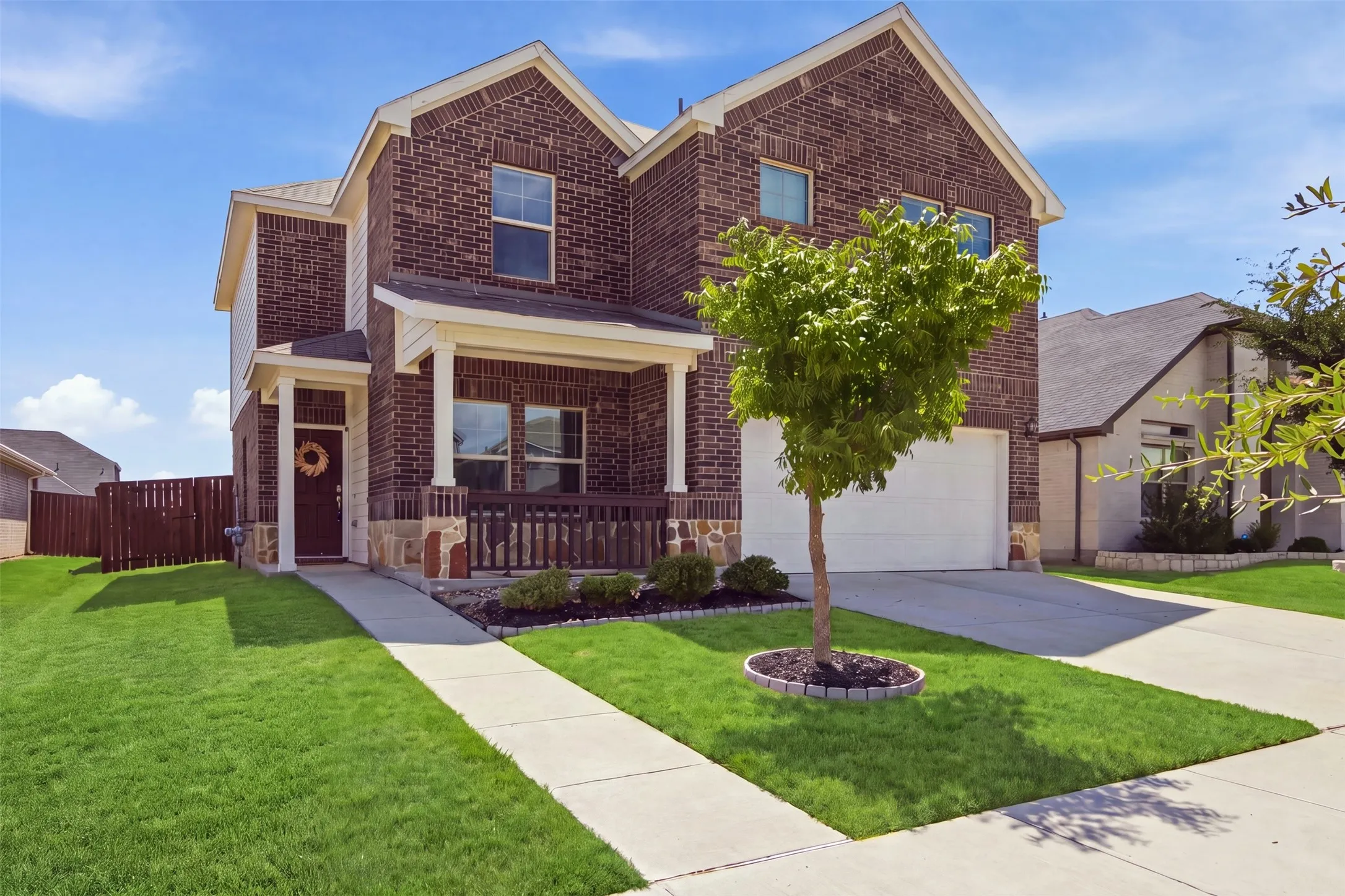 Brick exterior with stone accents, covered front porch, attached garage, concrete driveway, and established landscaping