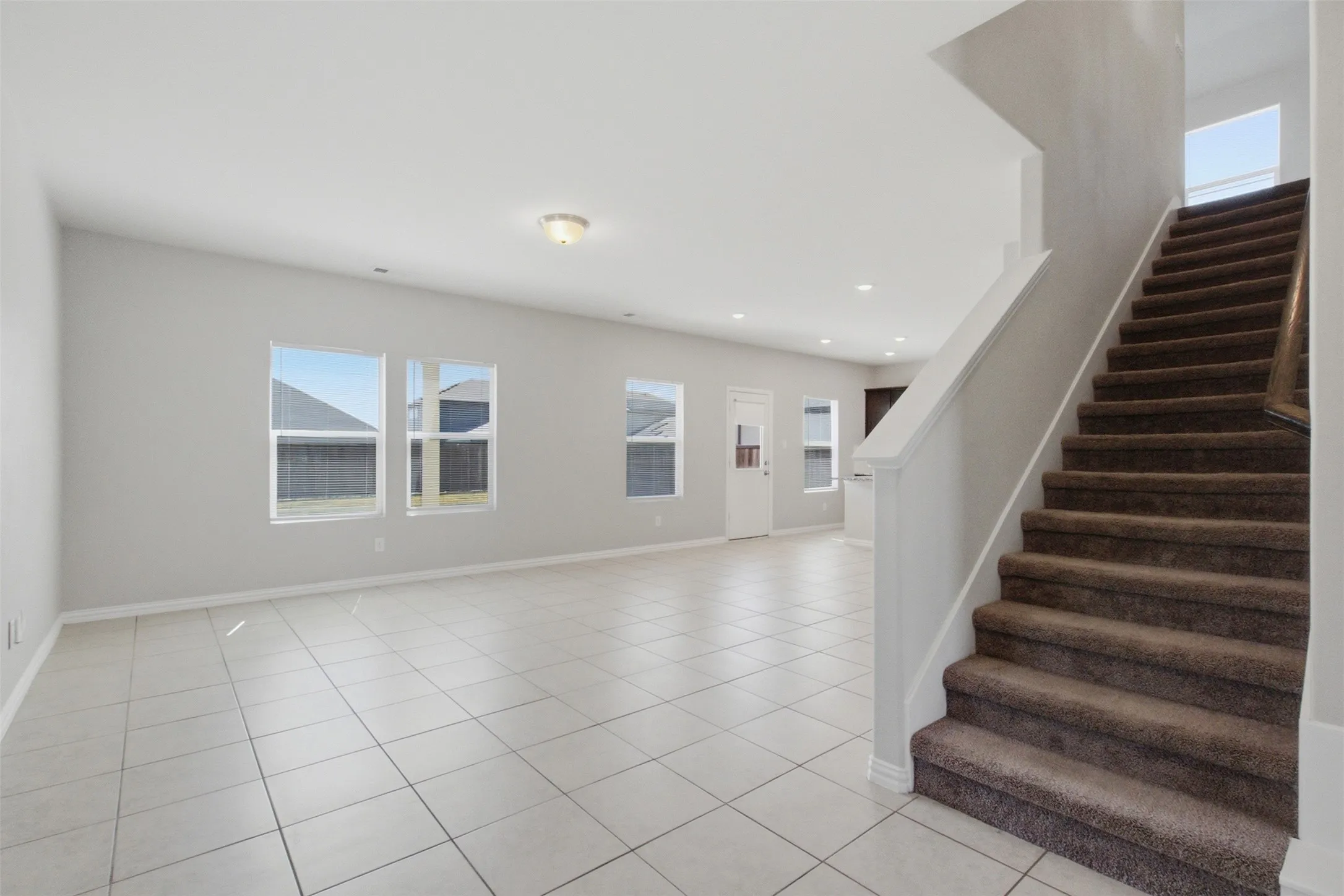 Spacious living area featuring light-toned tile flooring, recessed lighting, and multiple windows