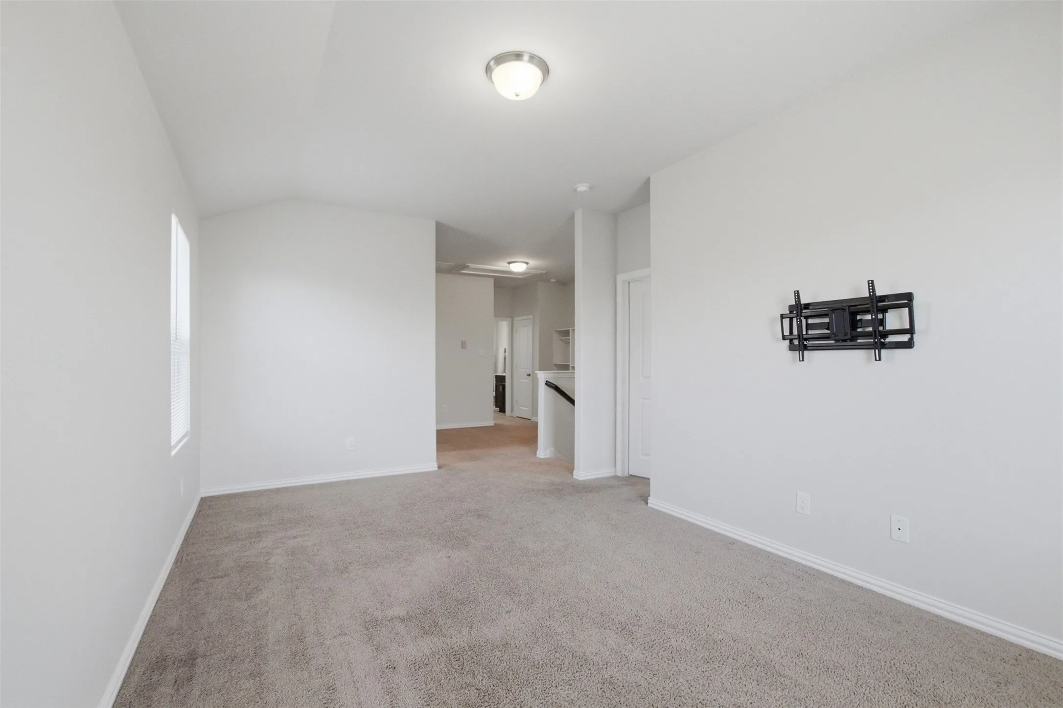 Neutral tone wall finishes, gray carpet flooring, recessed window, ceiling-mounted light fixture, and pre-installed television mount