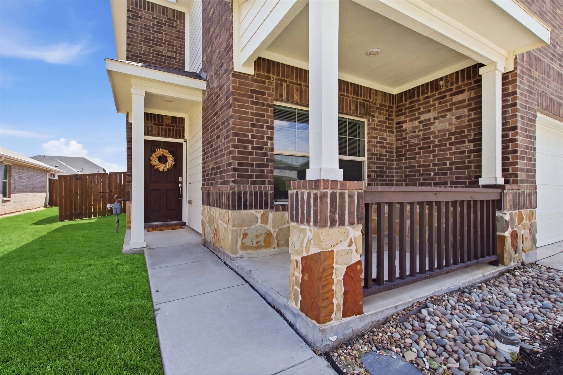 Brick facade with stone accents, covered front entry, concrete walkway, and landscaped rock bed