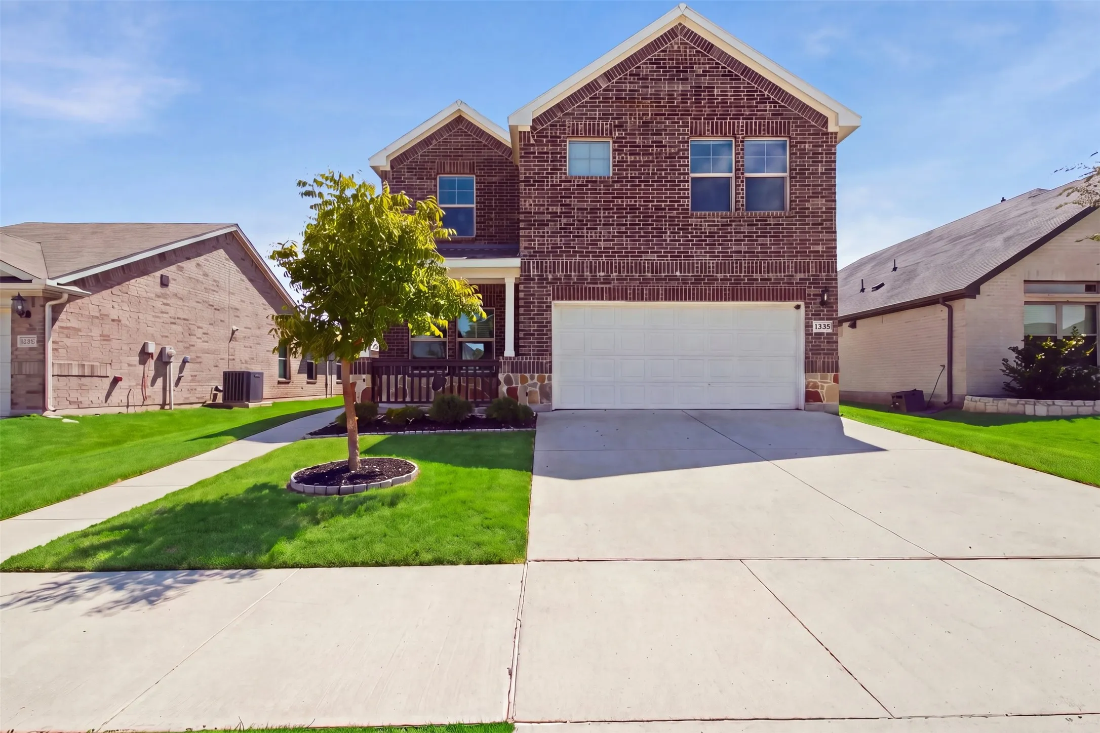 Two-story brick exterior with a white garage door, concrete driveway, and front porch