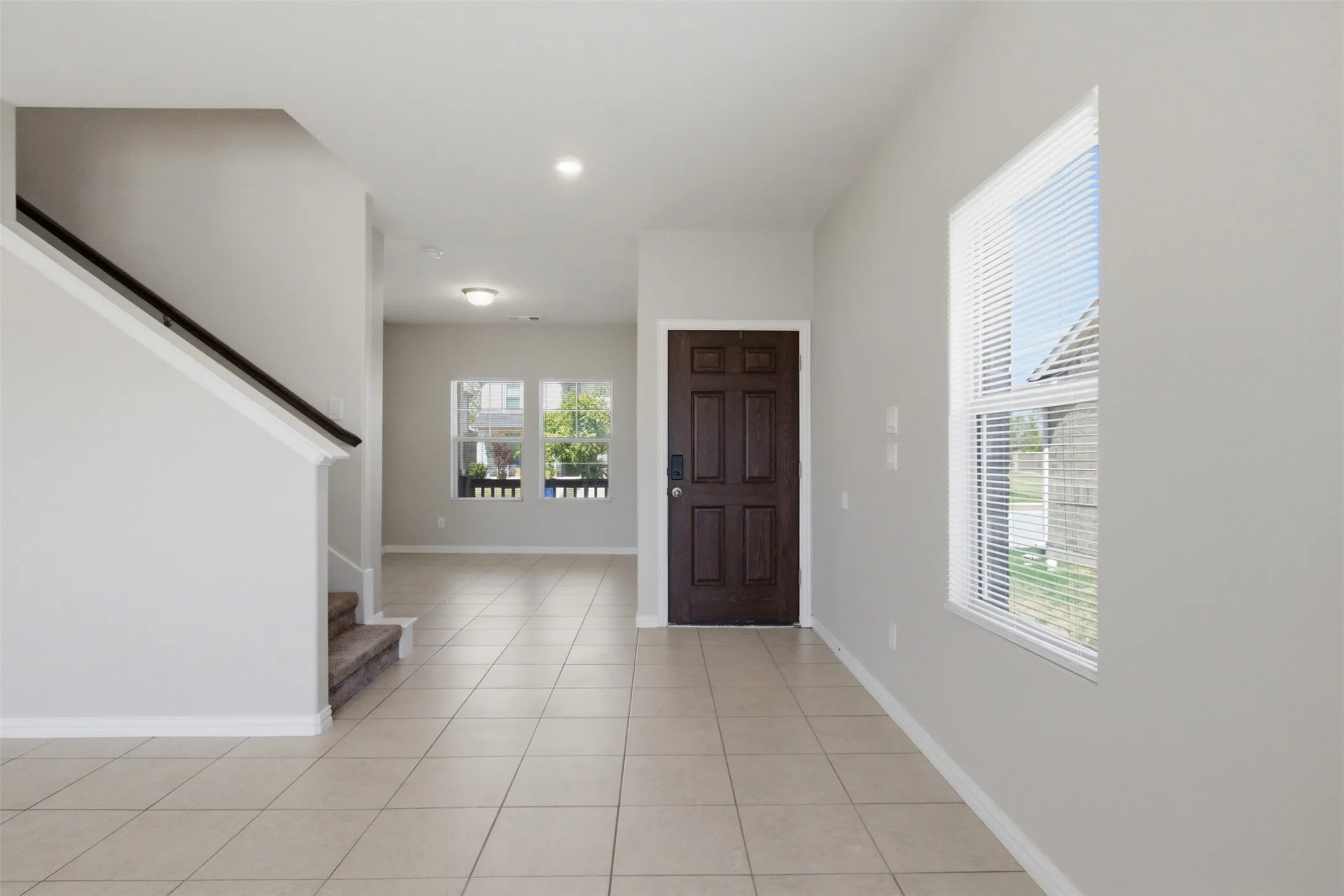Tile flooring, dark wood entry door, white trim, recessed lighting, and carpeted stairs