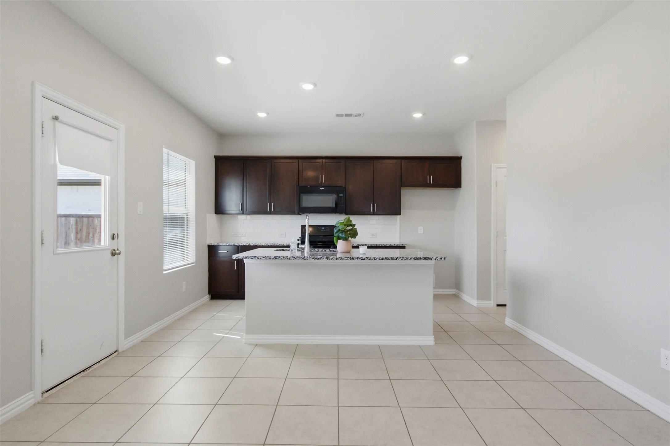 Kitchen featuring dark wood-finish cabinetry, a central island with a stone-finish countertop, stainless steel appliances, and a tile backsplash