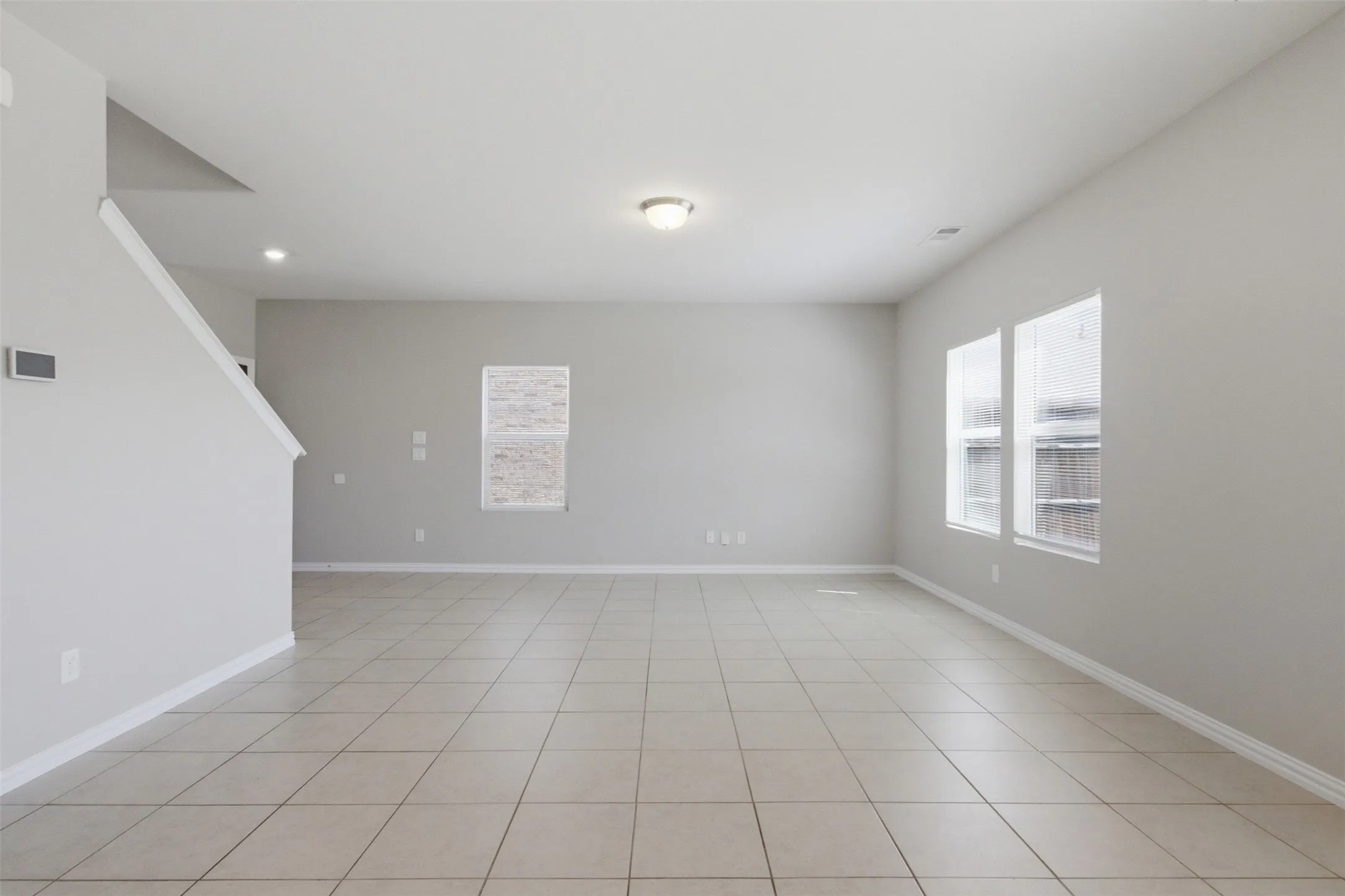 Spacious interior with neutral wall tones, large format tile flooring, multiple windows, and recessed lighting