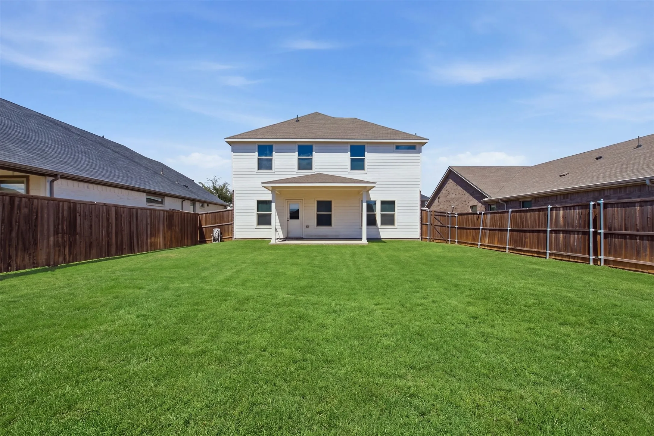 Expansive backyard with a manicured lawn, full privacy fencing, and a covered patio