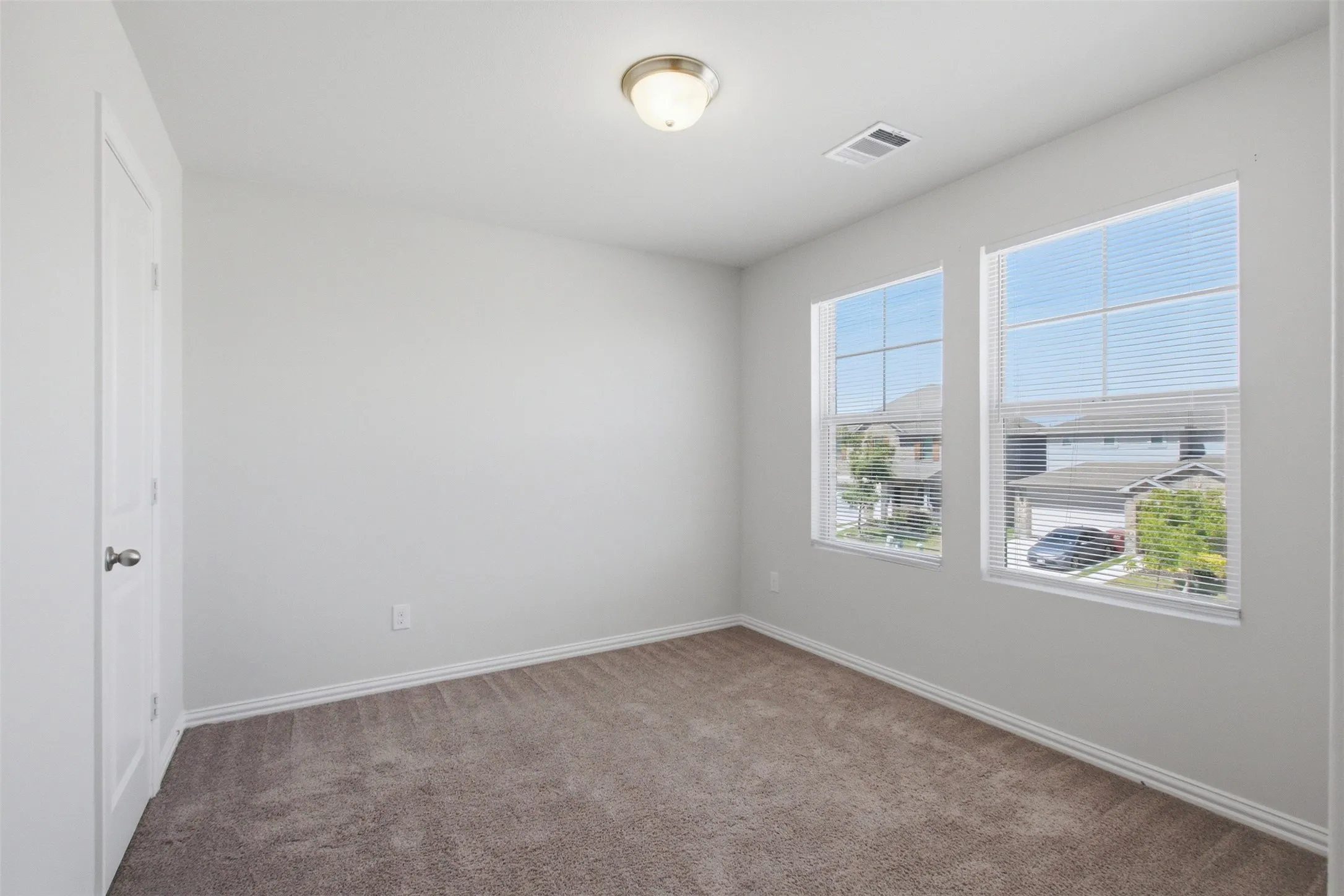 Neutral wall color, carpet flooring, two windows with blinds, white trim, and a flush-mount ceiling light fixture