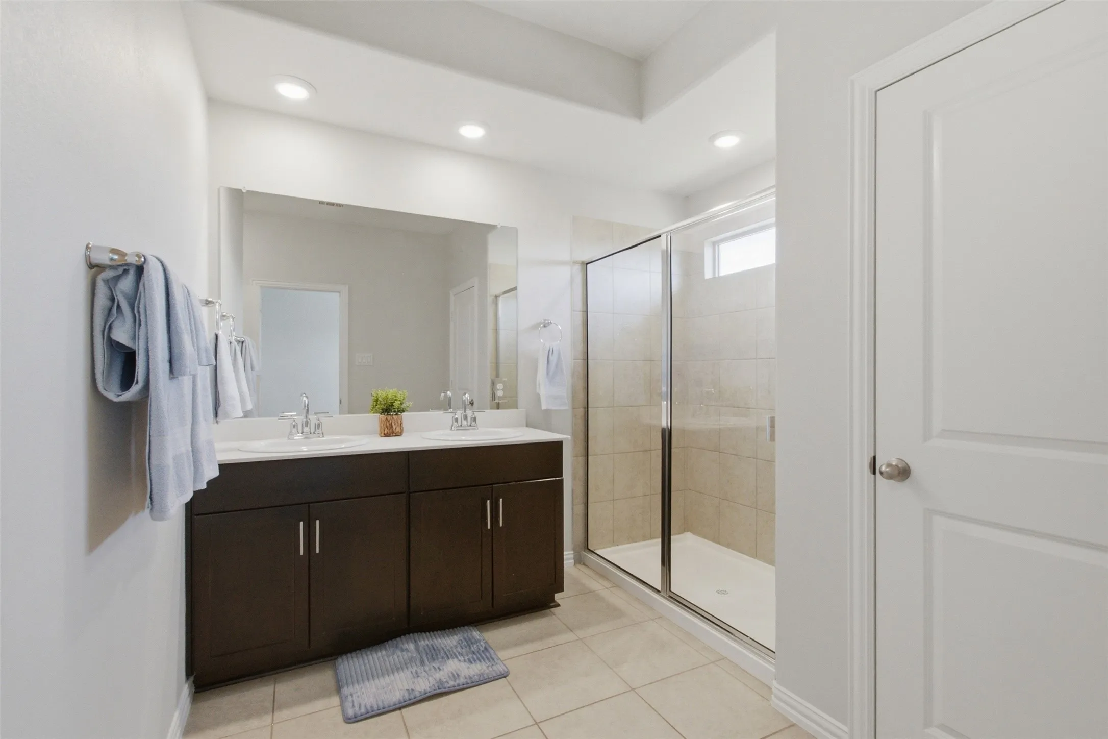 Dual vanity with dark wood-finish cabinetry, a large mirrored wall, and a glass-enclosed shower with tiled walls