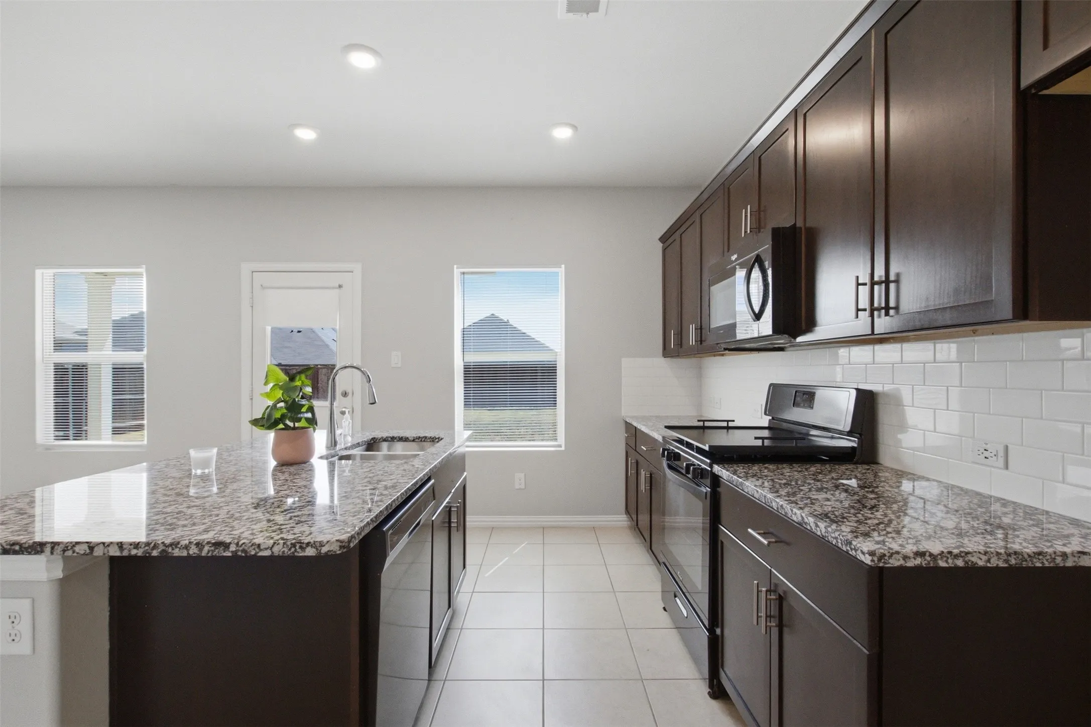 Kitchen featuring dark wood-finish cabinetry, granite countertops, subway tile backsplash, and a center island with an undermount sink