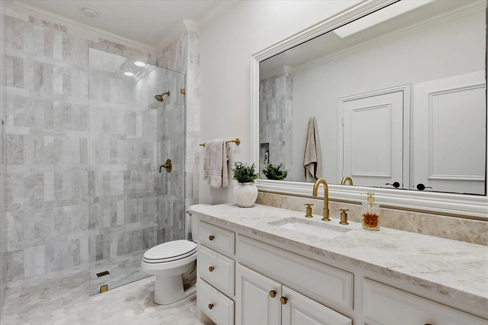 Marble tile, quartzite surfaces and polished brass fixtures elevate this remodeled ensuite bath.