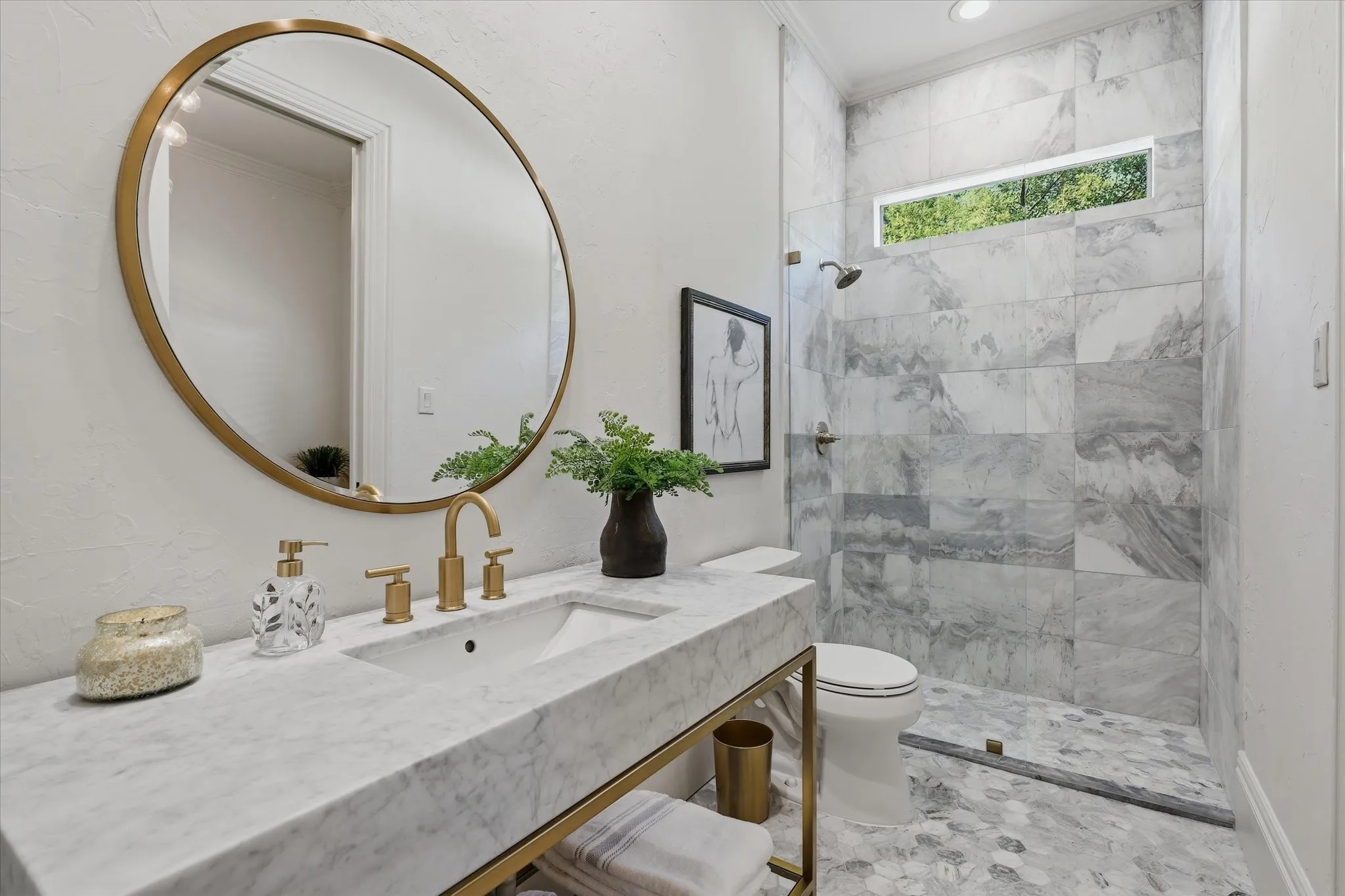 First floor guest ensuite bath is beautifully remodeled featuring marble finishes, a glass-enclosed shower and refined brass fixtures.