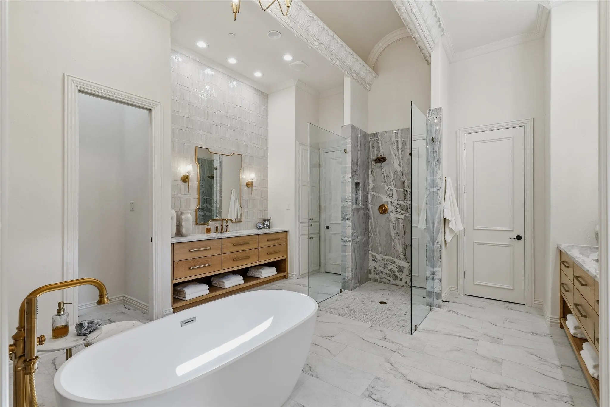 The remodeled primary bath pairs marble and quartzite with a sculptural soaking tub and glass-enclosed shower with dual shower heads.