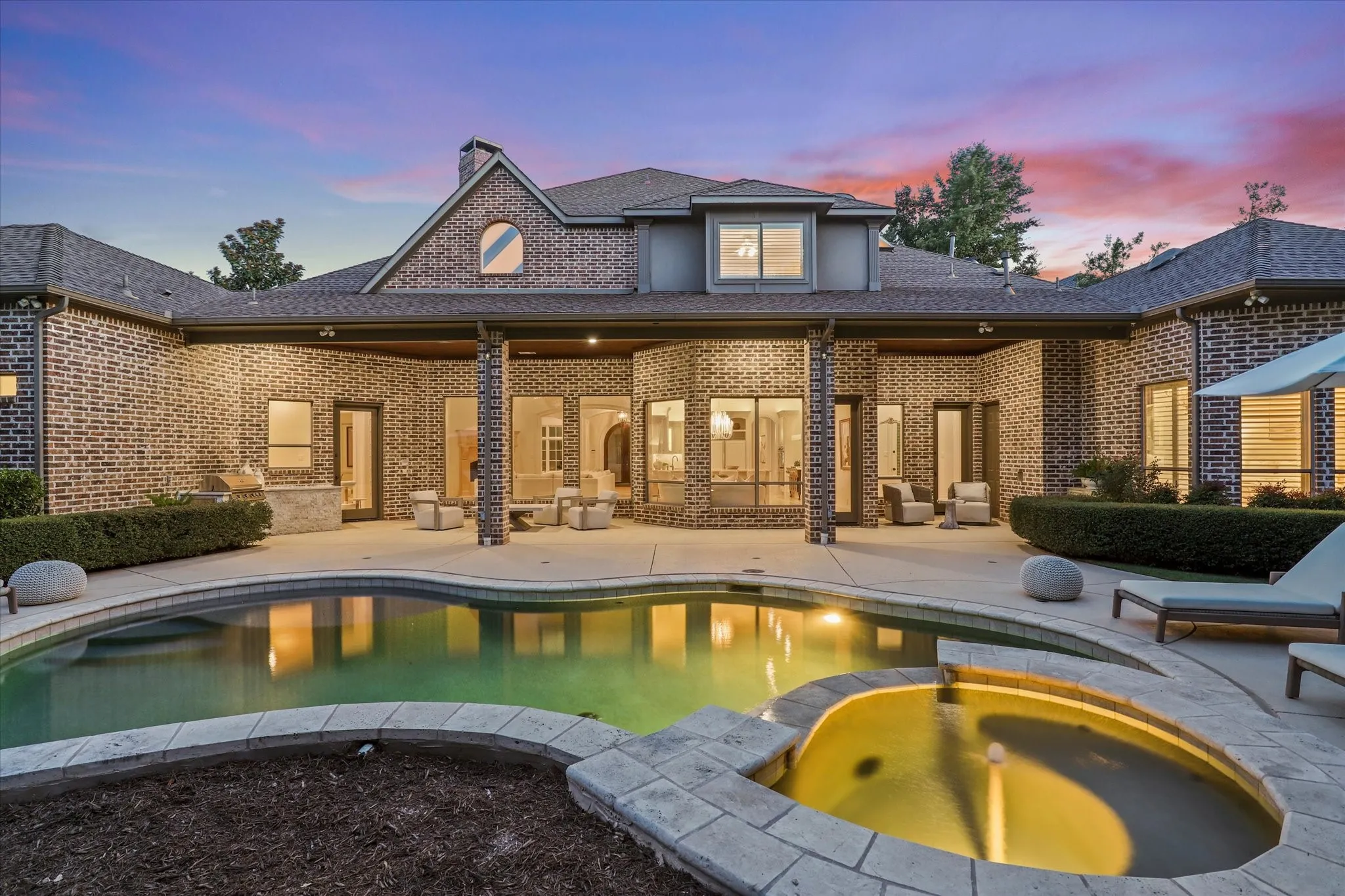 Twilight view of the home's backyard oasis with covered patio, sparkling, illuminated pool and spa.