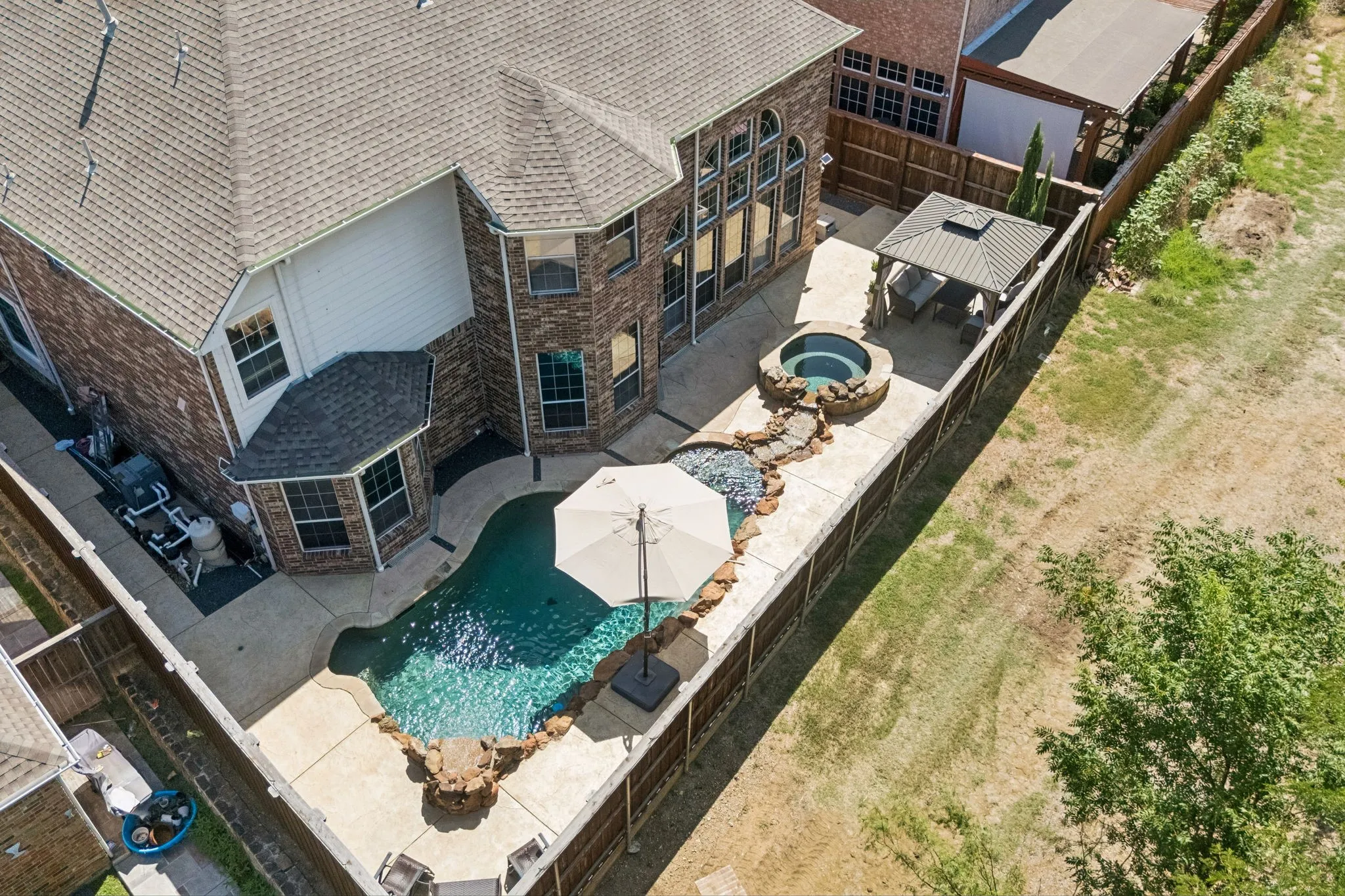 Aerial view captures the full backyard oasis, showcasing the pool, spa, outdoor living areas and private Greenbelt setting with mature trees beyond.