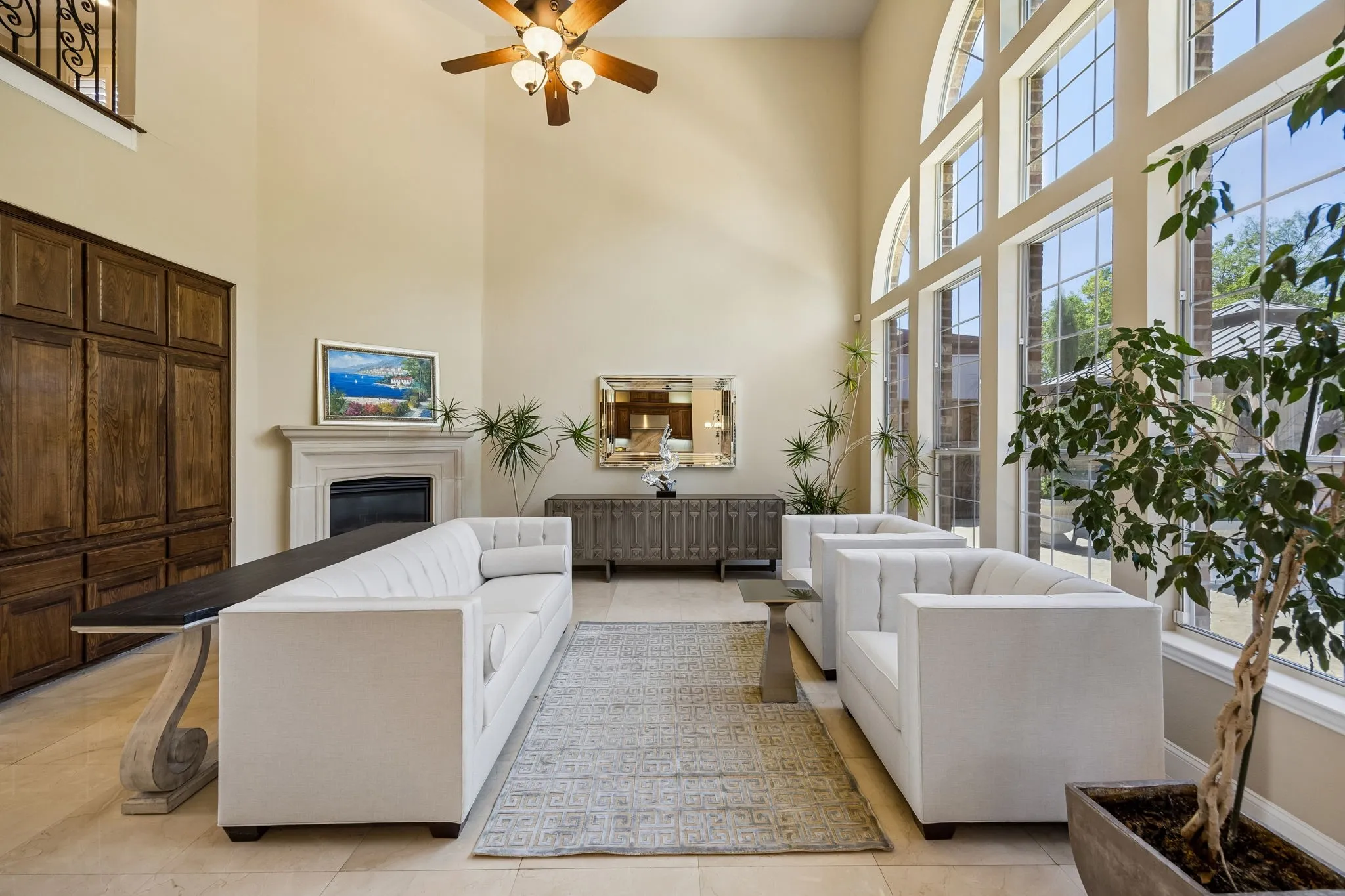An impressive two-story great room showcases soaring ceilings and a dramatic wall of windows that fills the space with natural light while offering beautiful views of the outdoor living area and sparkling pool. Elegant natural stone floors add a timeless, sophisticated touch, complemented by a Cast Stone fireplace and expansive living area ideal for both everyday enjoyment and entertaining.