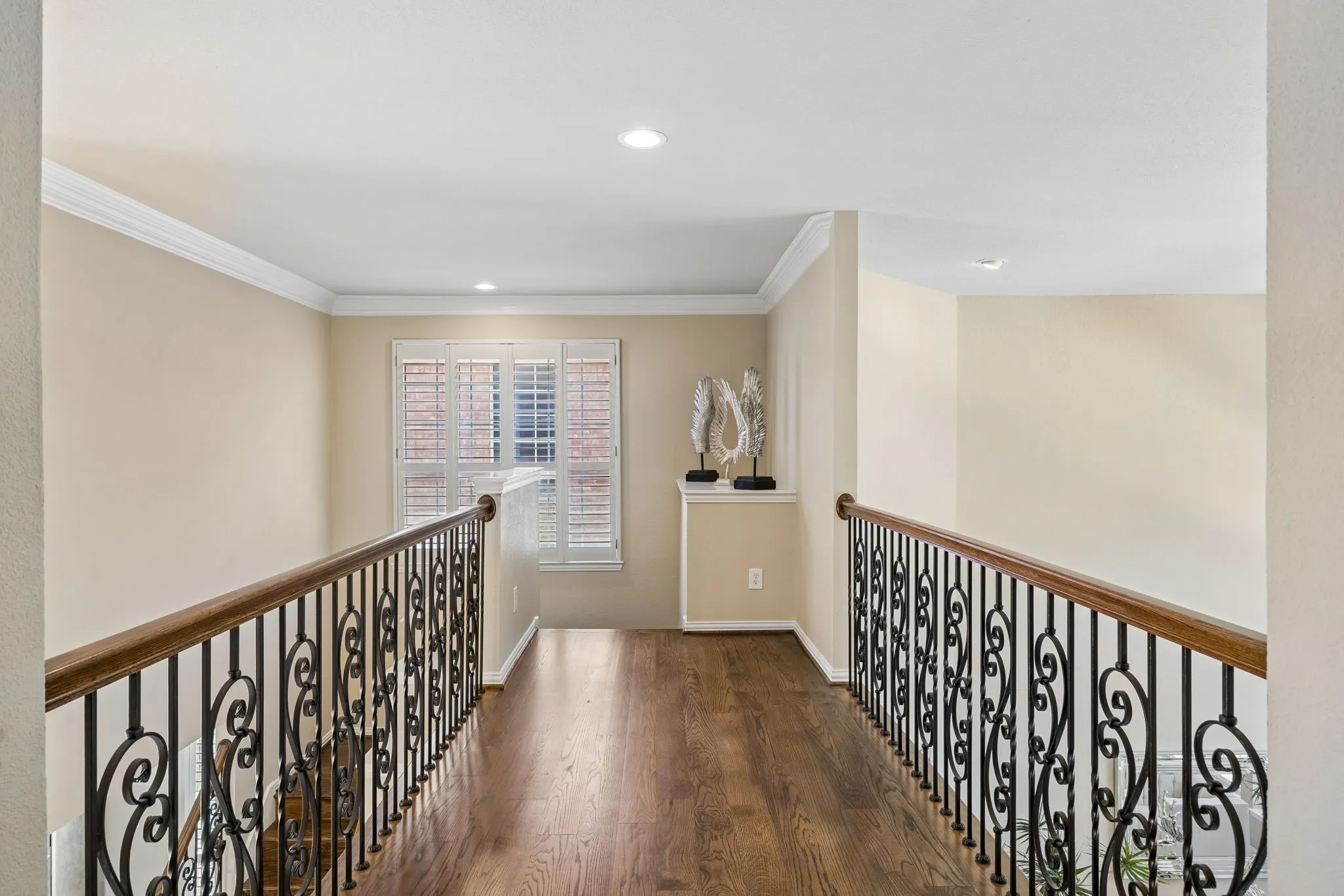 The upstairs catwalk features richly finished solid hardwood floors and decorative wrought iron balusters, creating an elegant connection between the home's upper-level spaces.  Expansive views toward both the front and back of the home overlook the two-story living area, highlighted by an impressive collection of arched windows framing the outdoor setting.