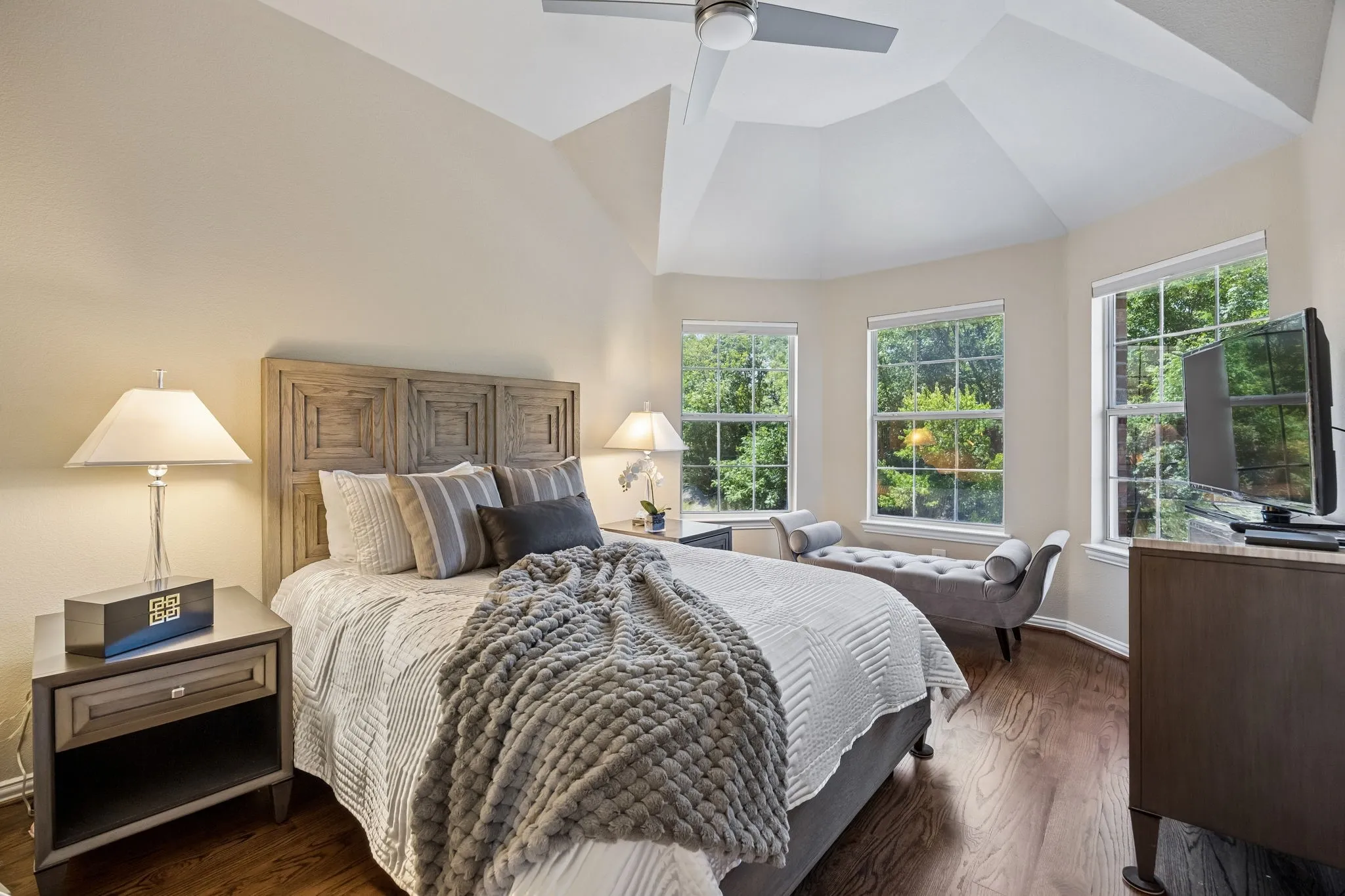 This spacious upstairs bedroom features solid hardwood floors, designer paint color, vaulted ceiling, and multiple windows showcasing peaceful views of the pool and Greenbelt, with the hall bathroom conveniently located nearby.
