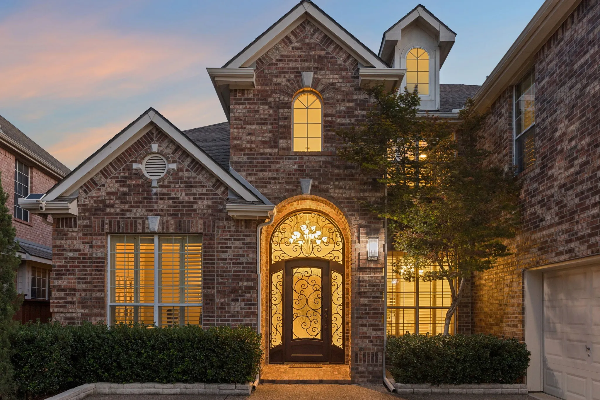 Beautifully captured at twilight, the home glows beneath the soft evening sky, highlighting its stately entry, warm exterior lighting, and impressive curb appeal.